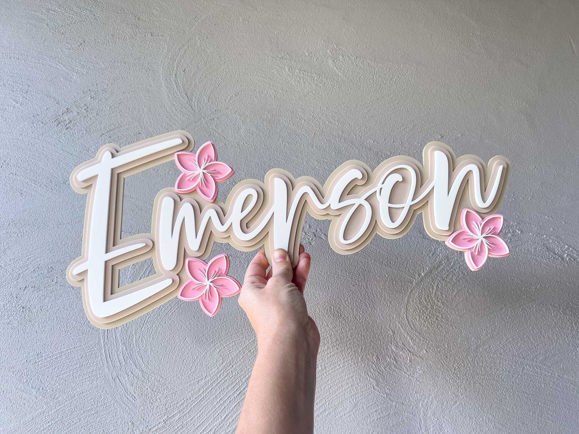 Tropical paradise frangipani triple layer acrylic name plaque that says 'Emerson' in shades of brown and beige with light pink frangipanis.