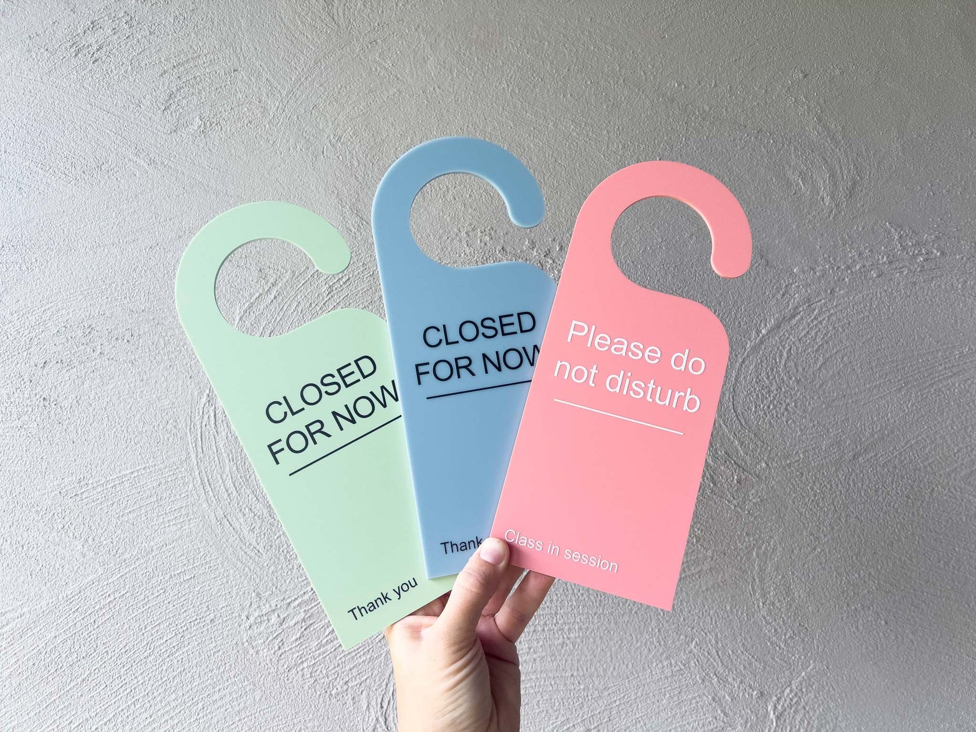 Three colorful door hangers with text held against a gray wall | Coji Designs