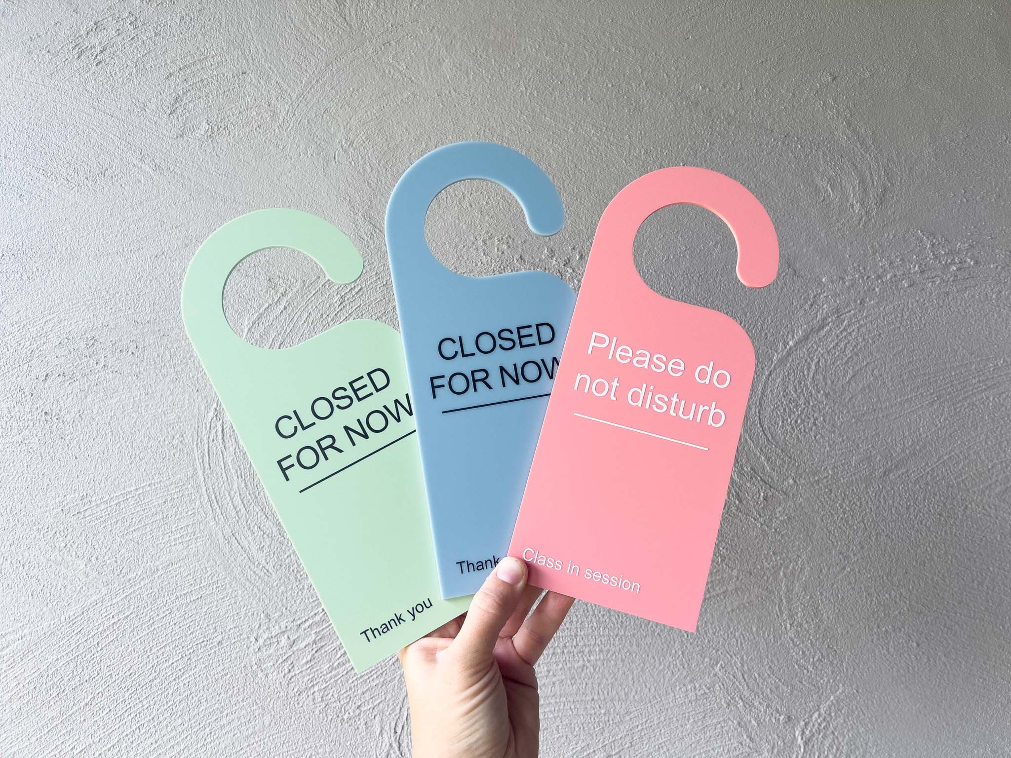 Three colorful door hangers with text held against a gray wall | Coji Designs