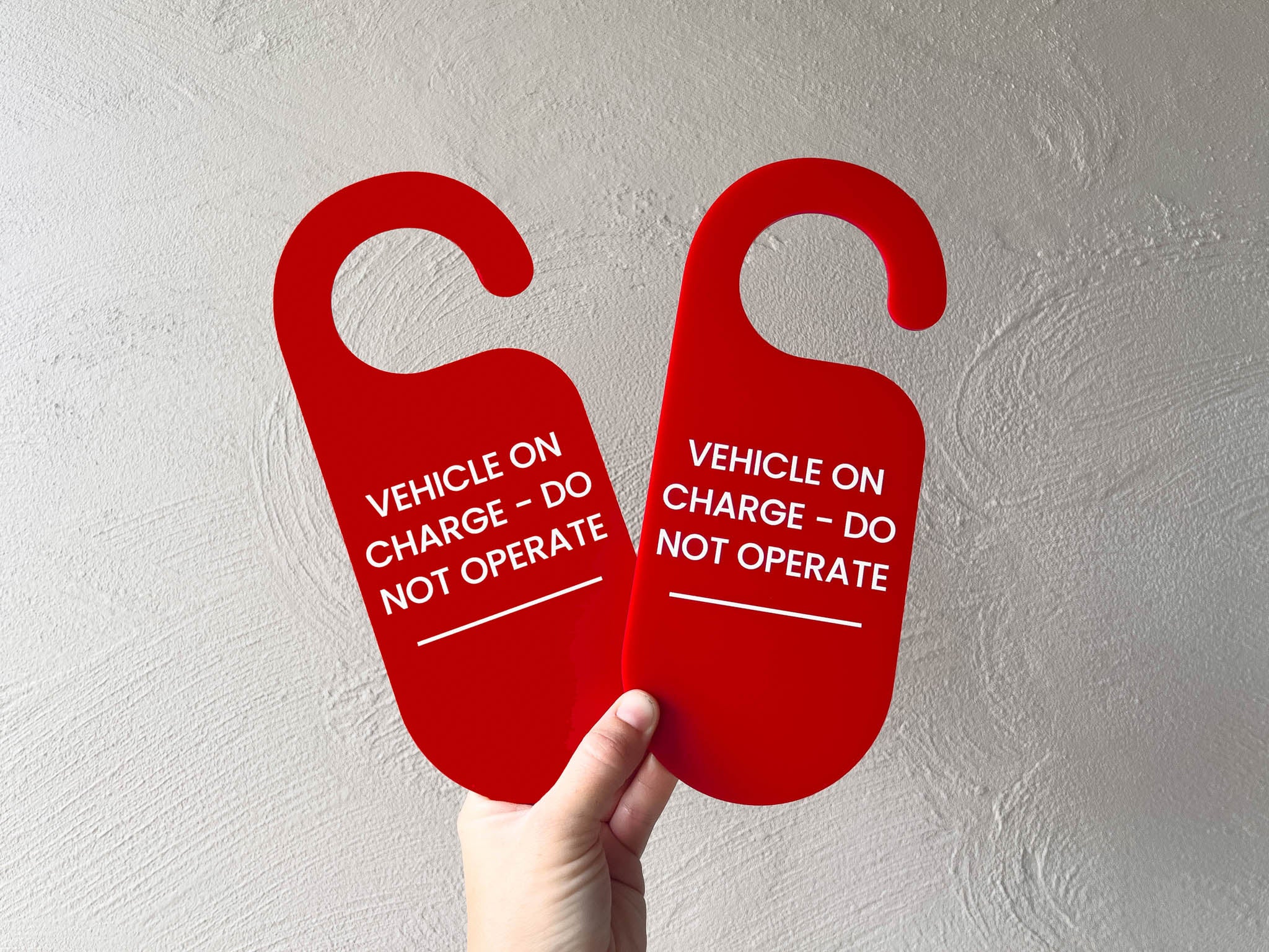 Custom printed red rounded edge hangers for hanging in a vehicle. The hangers read 'VEHICLE ON CHARGE - DO NOT OPERATE'.