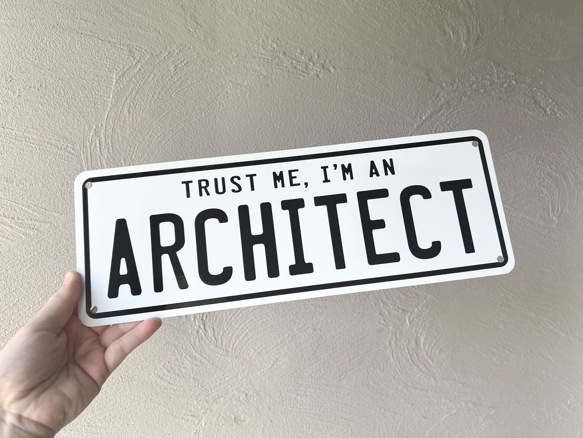 Hand holding a sign that reads 'Trust me, I'm an architect' against a plain background
