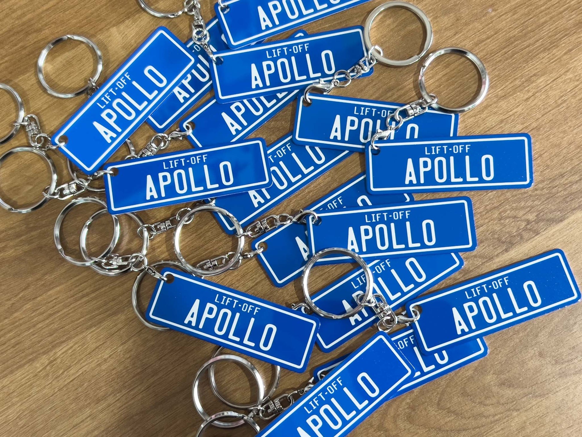 Multiple blue 'APOLLO' keychains on a wooden surface