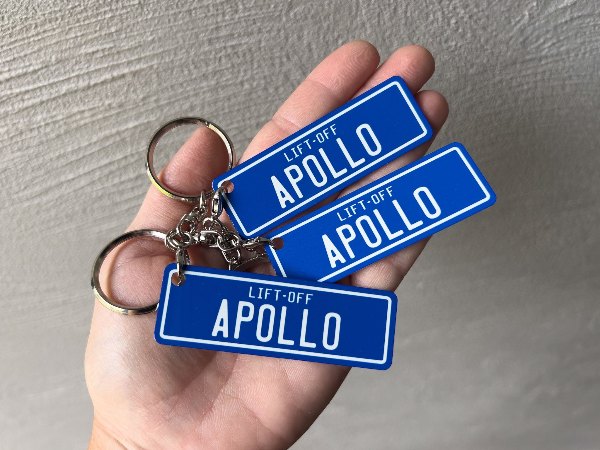 Custom printed royal blue and white aluminium keychains that read 'lift-off Apollo'.