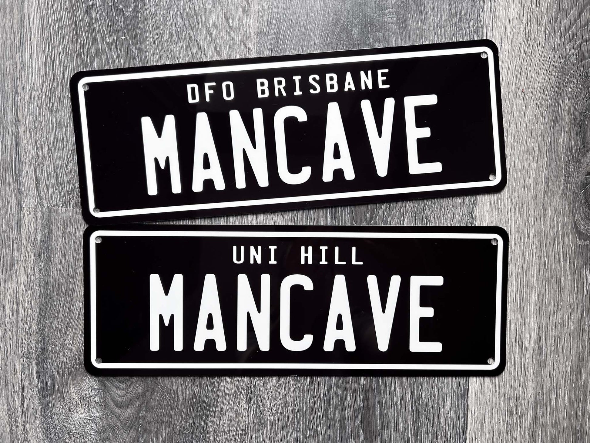 Two black rectangular signs with white text that say 'DFO BRISBANE MANCAVE'.