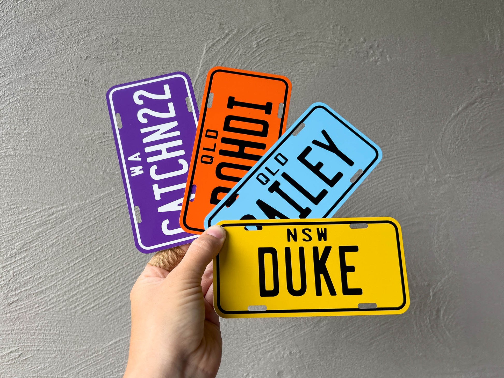 Four small license plate-style signs held by a hand against a grey background