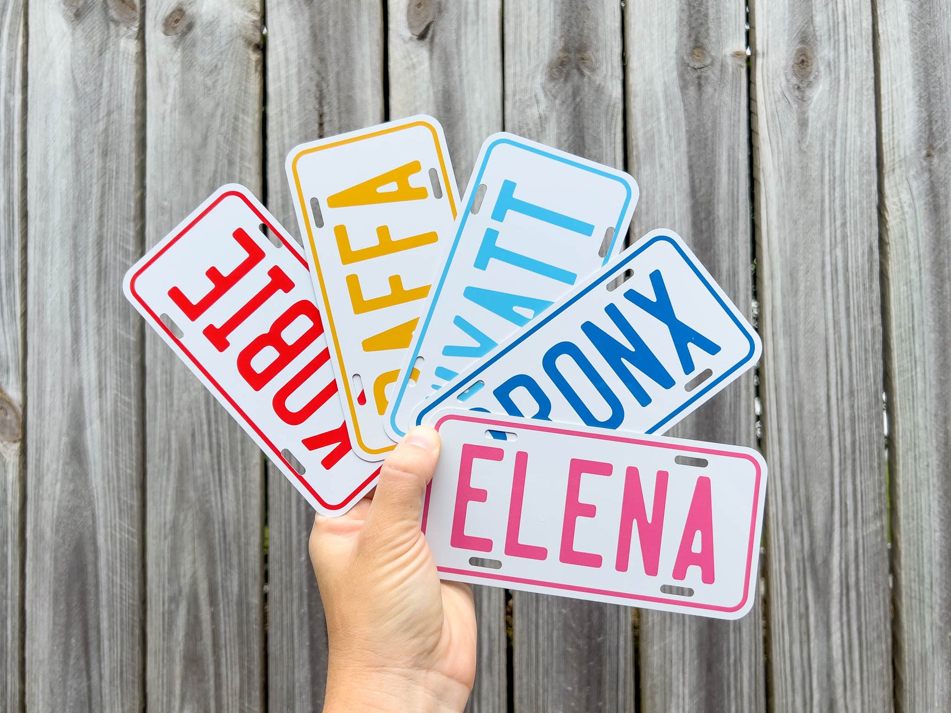 Hand holding personalised mini name plates with different names against a wooden background