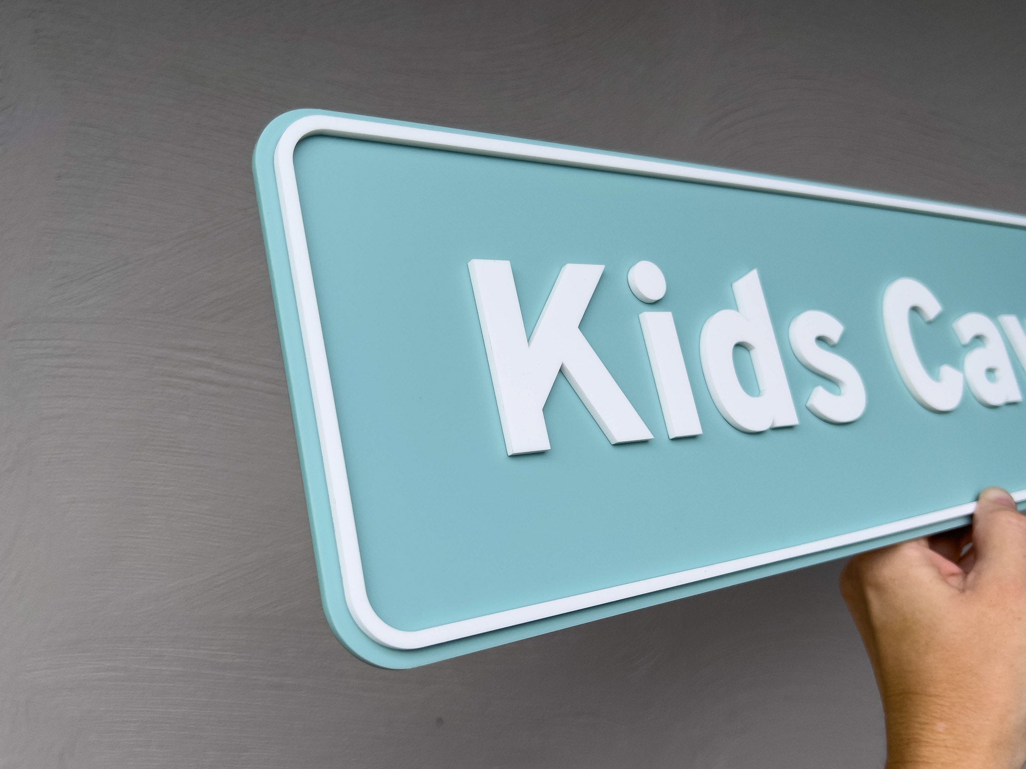 Hand holding a teal sign with 'Kids Care' on a gray background | Coji Designs
