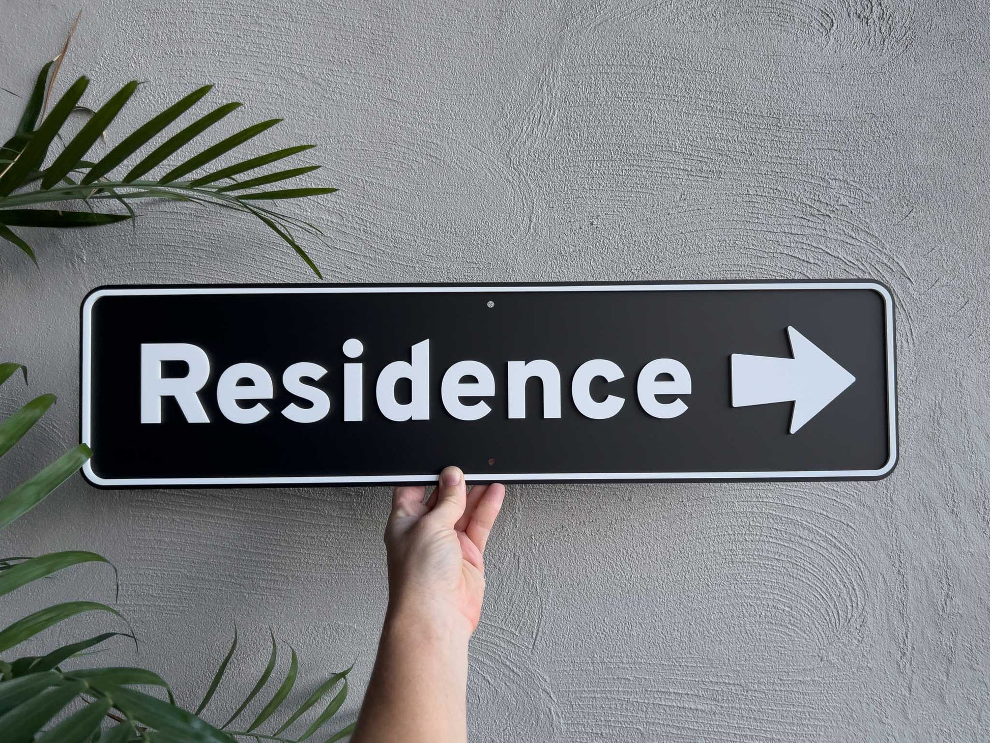 Hand holding a 'Residence' sign with an arrow on a gray wall | Coji Designs