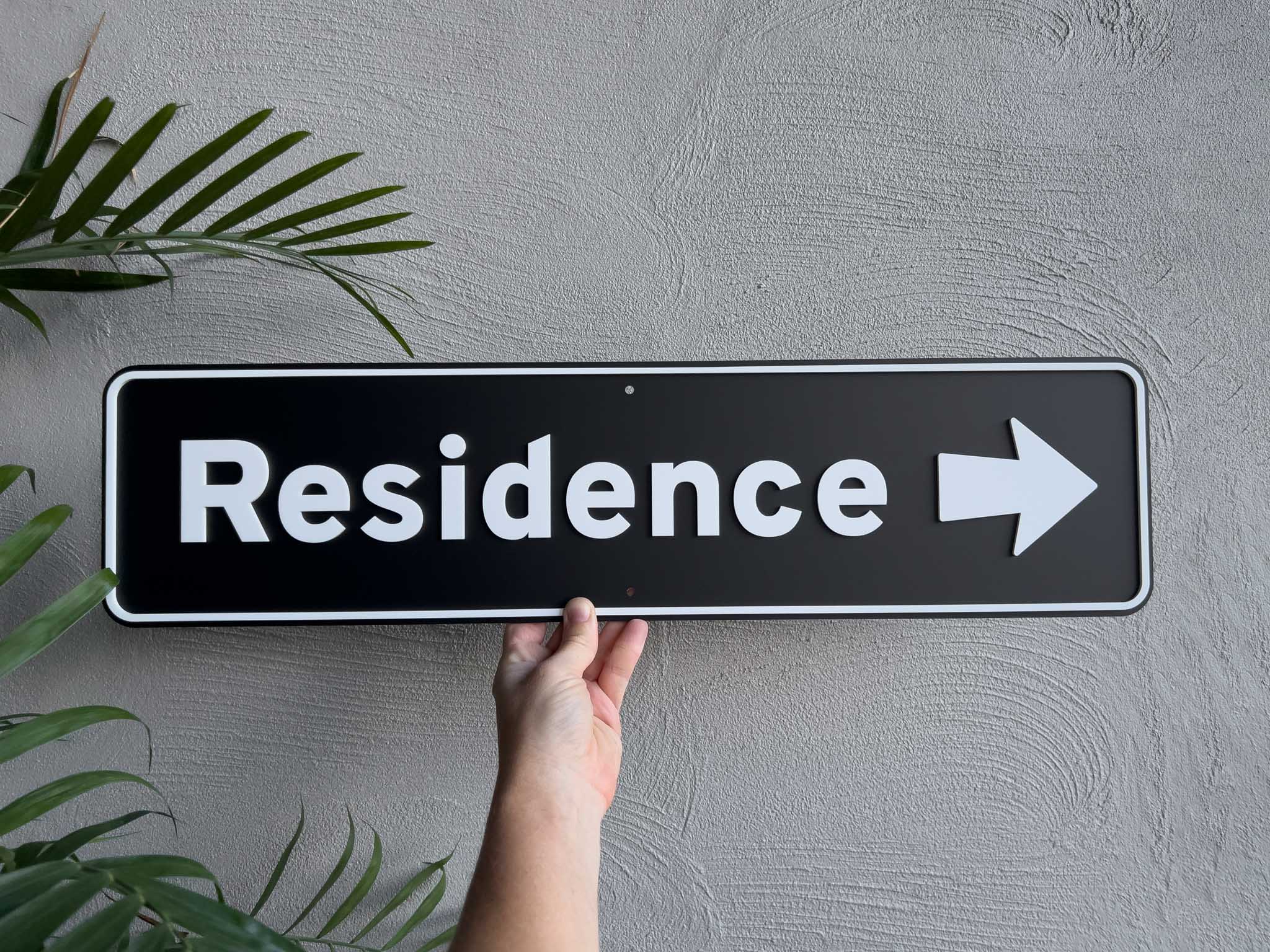 Hand holding a 'Residence' sign with an arrow on a gray wall | Coji Designs