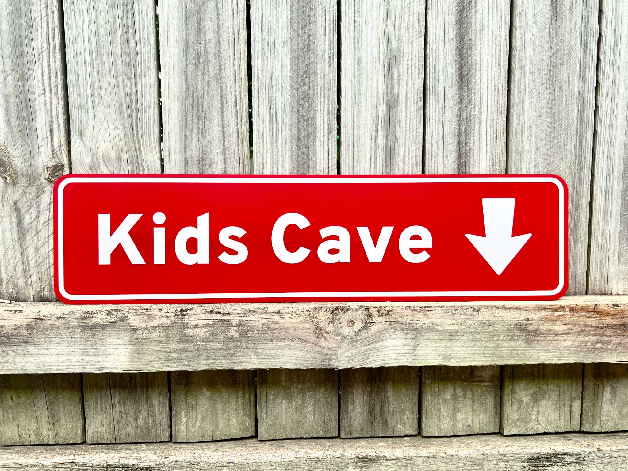 Red sign with 'Kids Cave' and an arrow pointing downwards on a wooden background