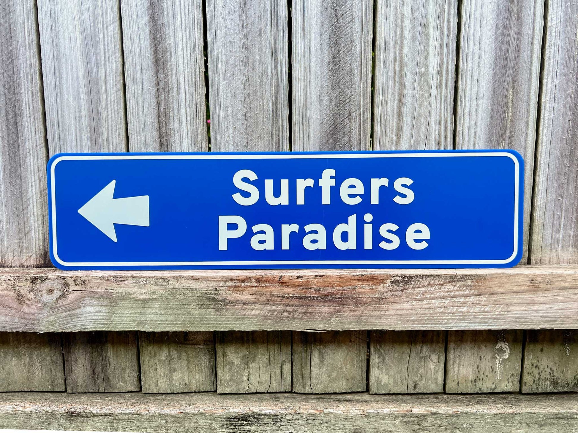 Personalised novelty direction sign that says 'Surfers Paradise' in a coastal blue colour pointing to the left.