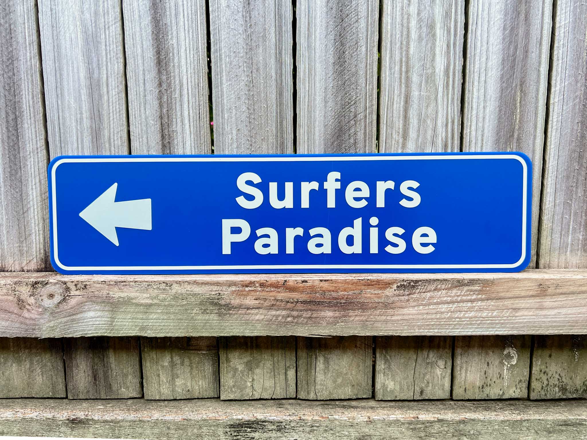 Personalised novelty direction sign that says 'Surfers Paradise' in a coastal blue colour pointing to the left.