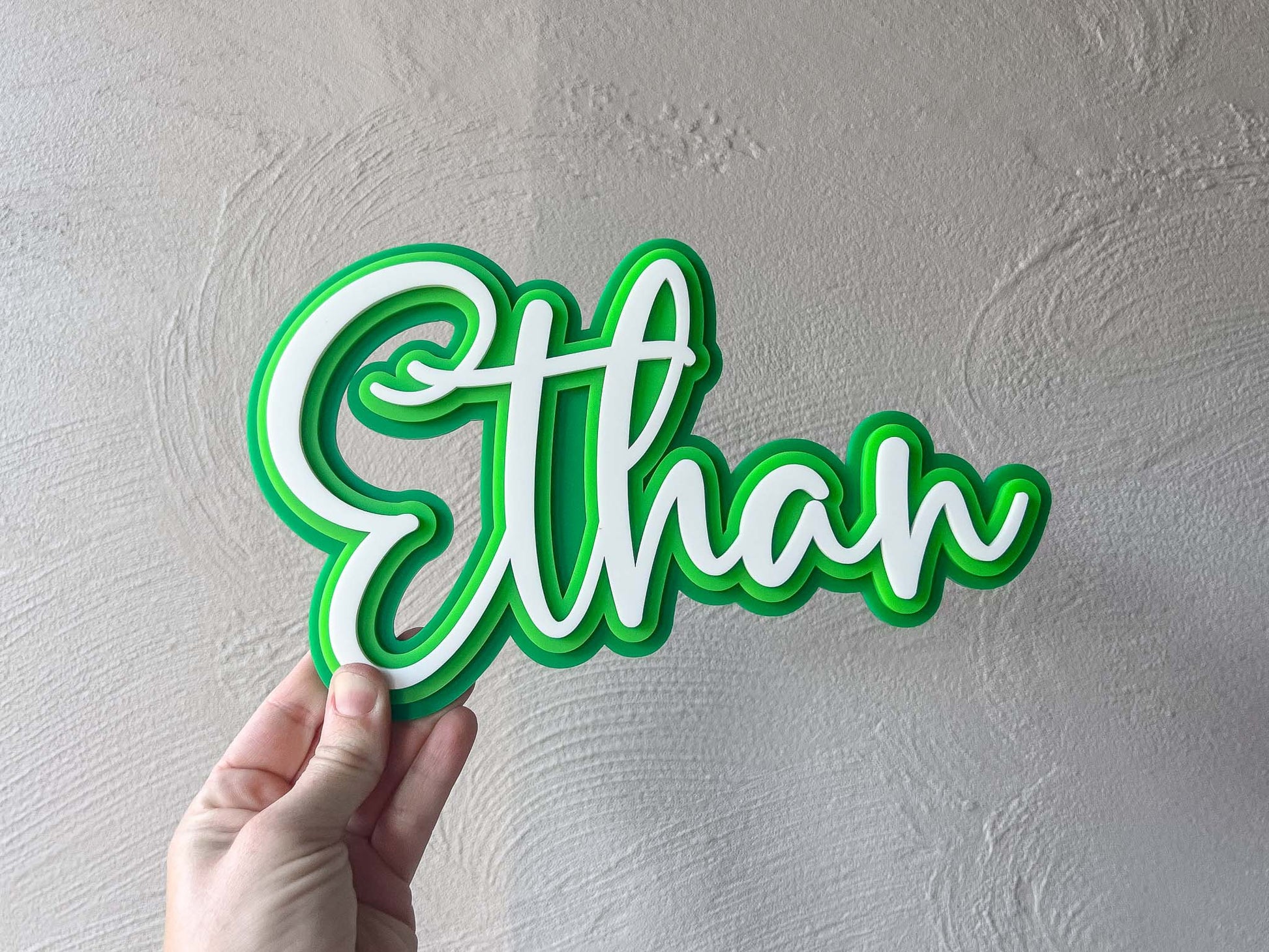 Hand holding a bright green and white personalised laser cut name plaque that reads 'Ethan'.