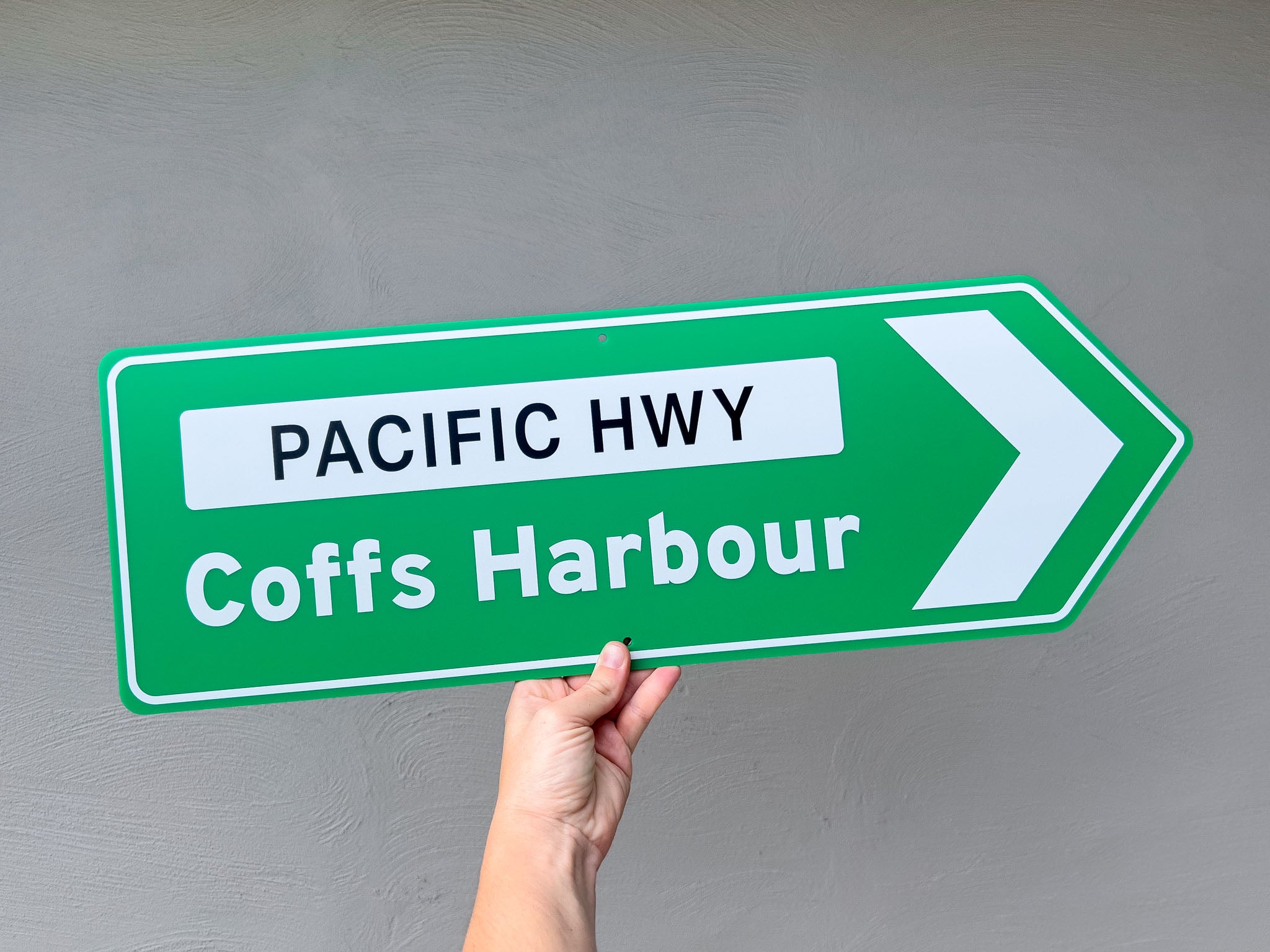 Classic green novelty highway road sign pointing to Pacific Hwy and Coffs Harbour against a grey background