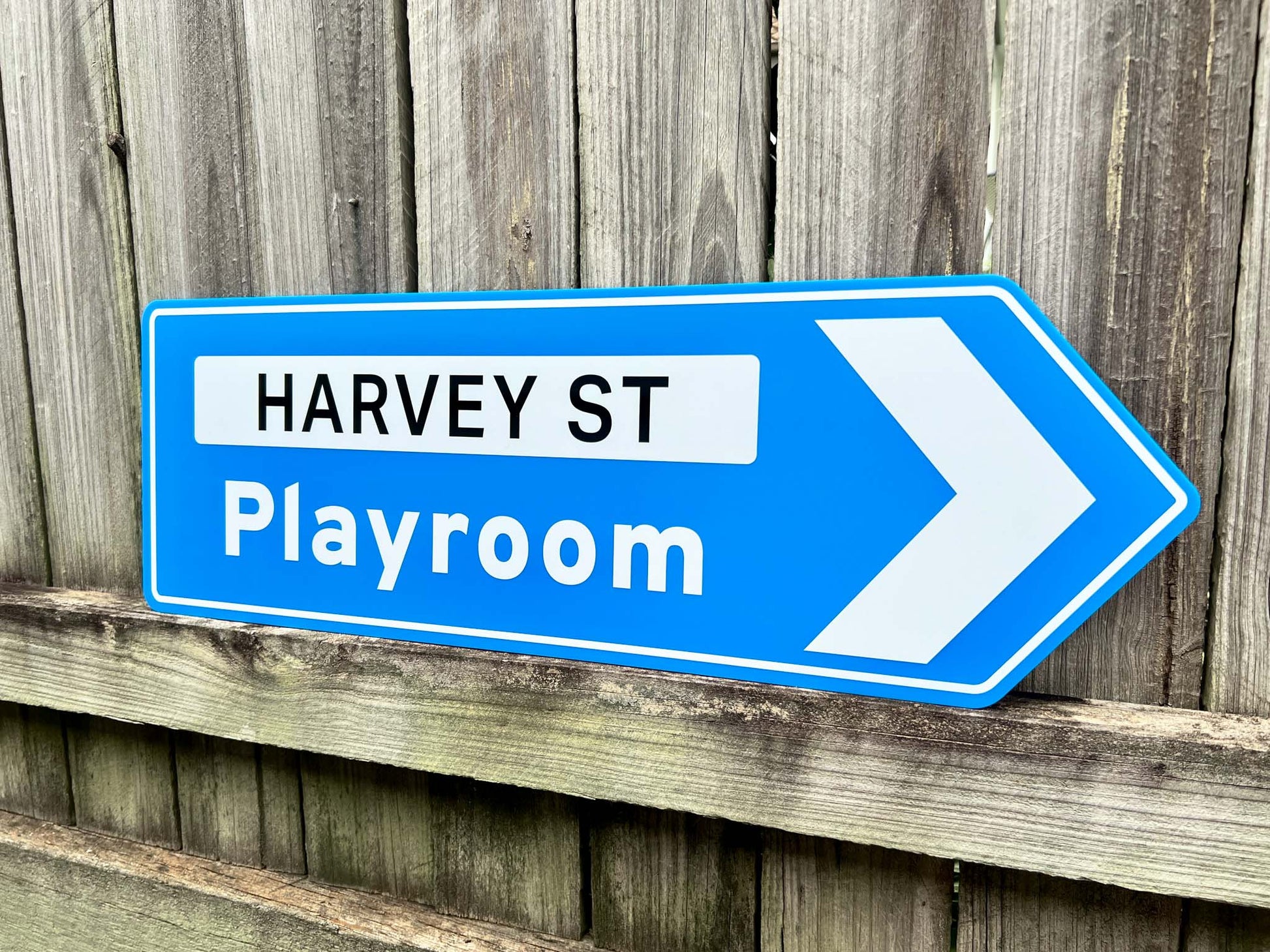 Blue sign pointing to 'Harvey St Playroom' against a wooden fence background