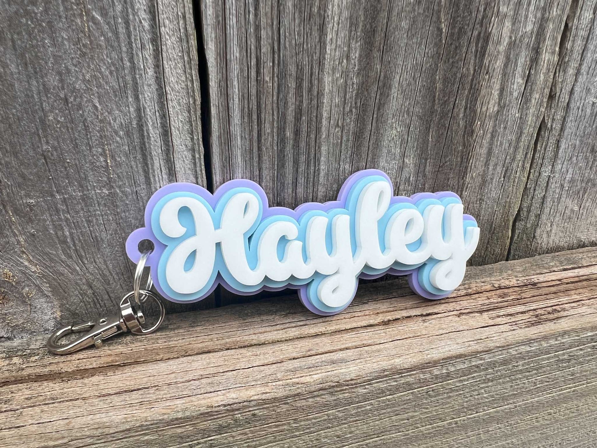 A cute bubbly font style keychain made from 3 layers of acrylic that reads 'Hayley' in light blue, purple and white.