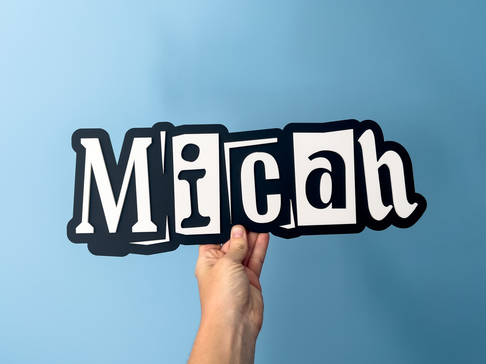 Hand holding a custom made acrylic layed sign in black and white thay says 'Micah..