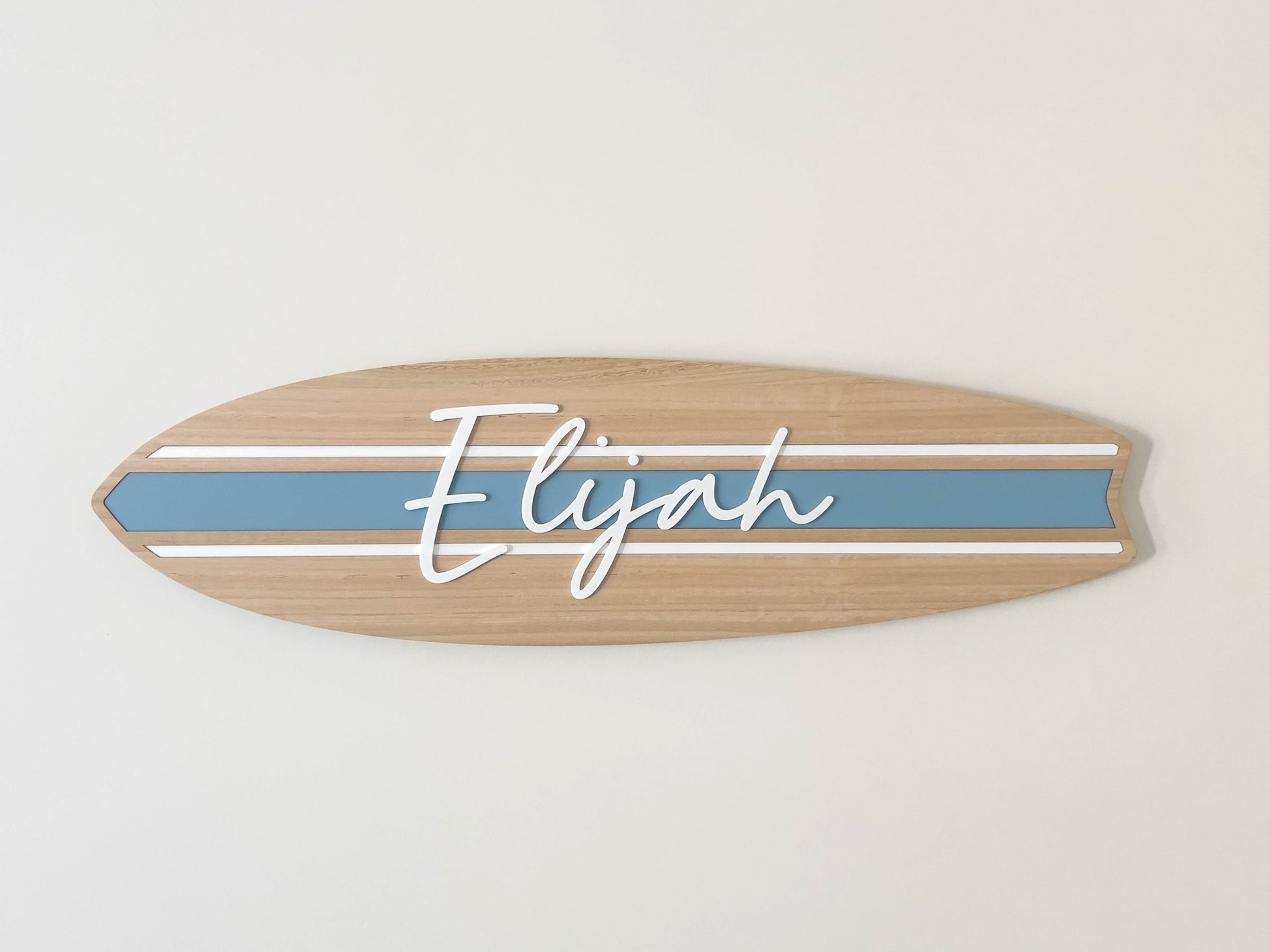 Custom wooden surfboard-shaped name plaque with 'Elijah' mounted on a white bedroom wall.