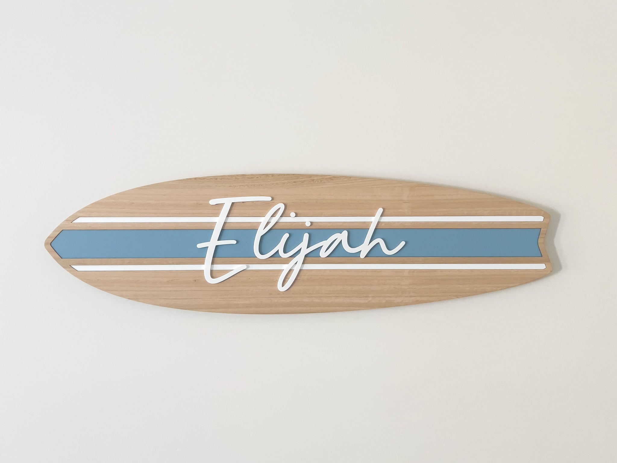 Custom wooden surfboard-shaped name plaque with 'Elijah' mounted on a white bedroom wall.