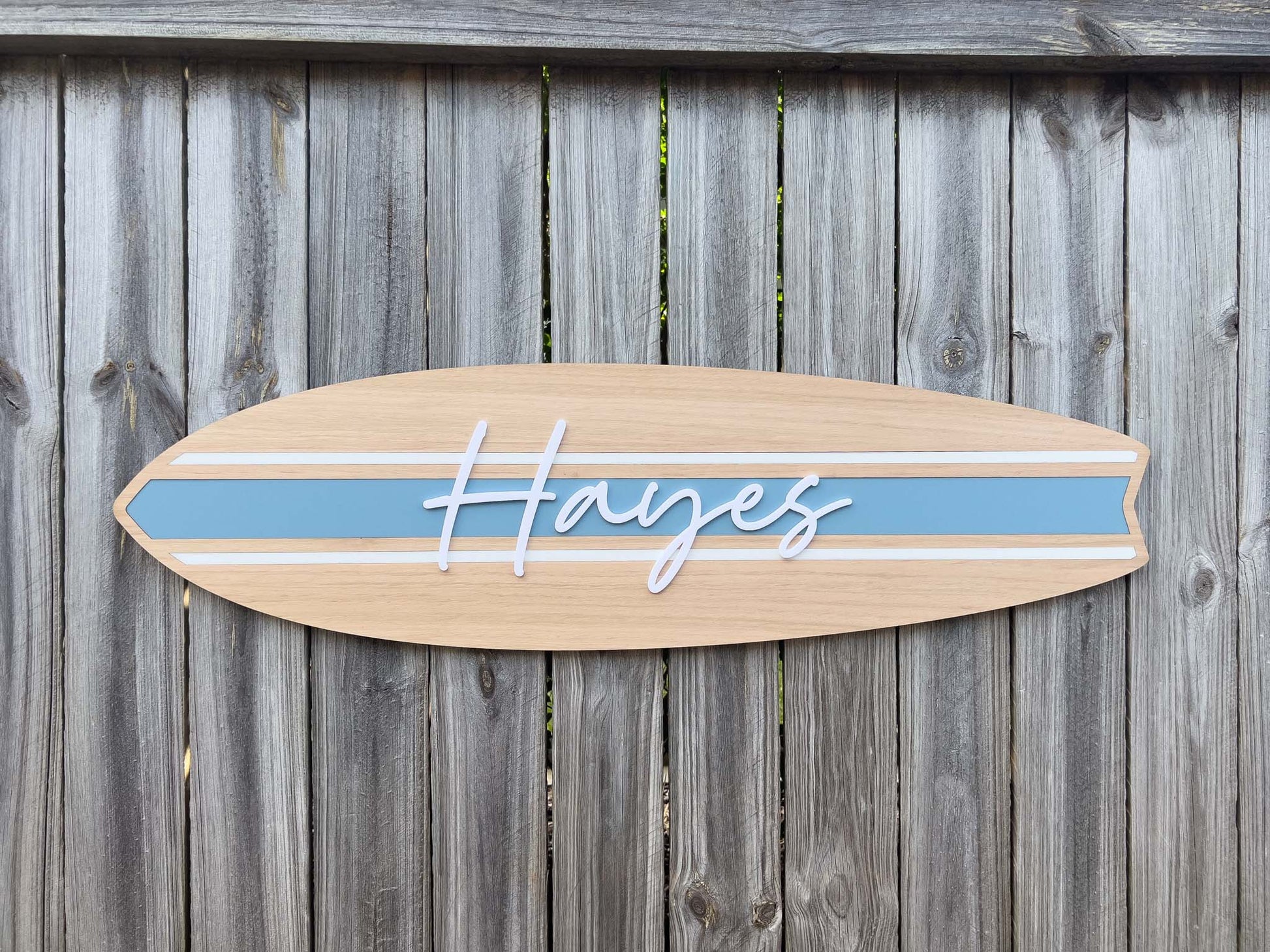 Wooden surfboard-shaped sign with 'Hayes' in white 3D acrylic lettering and a coastal dusty blue stripe.