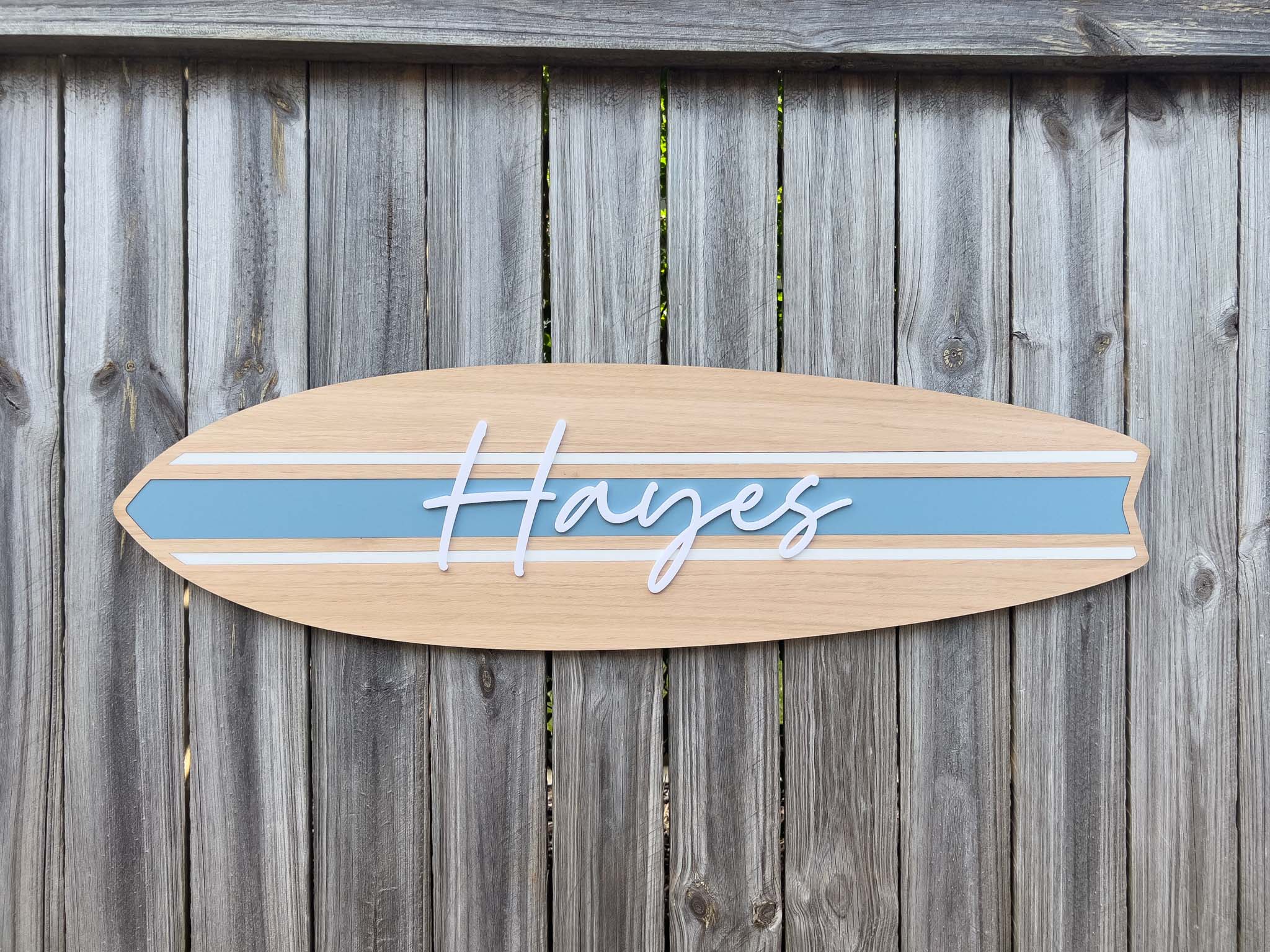 Wooden surfboard-shaped sign with 'Hayes' in white 3D acrylic lettering and a coastal dusty blue stripe.