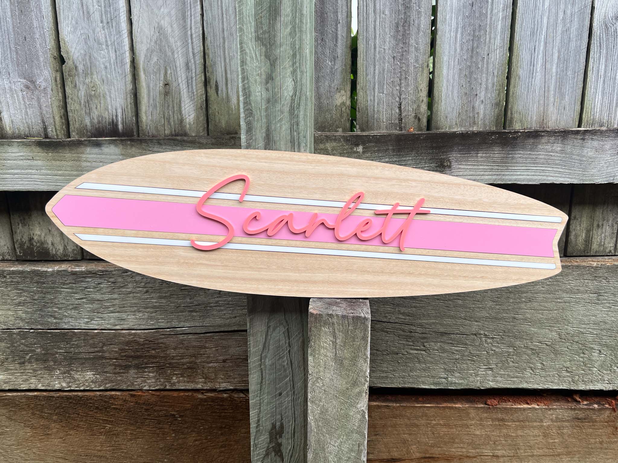 A coastal style timber name plaque made of wood and acrylic with the name 'Scarlett' in a melon pink with a light pink stripe.