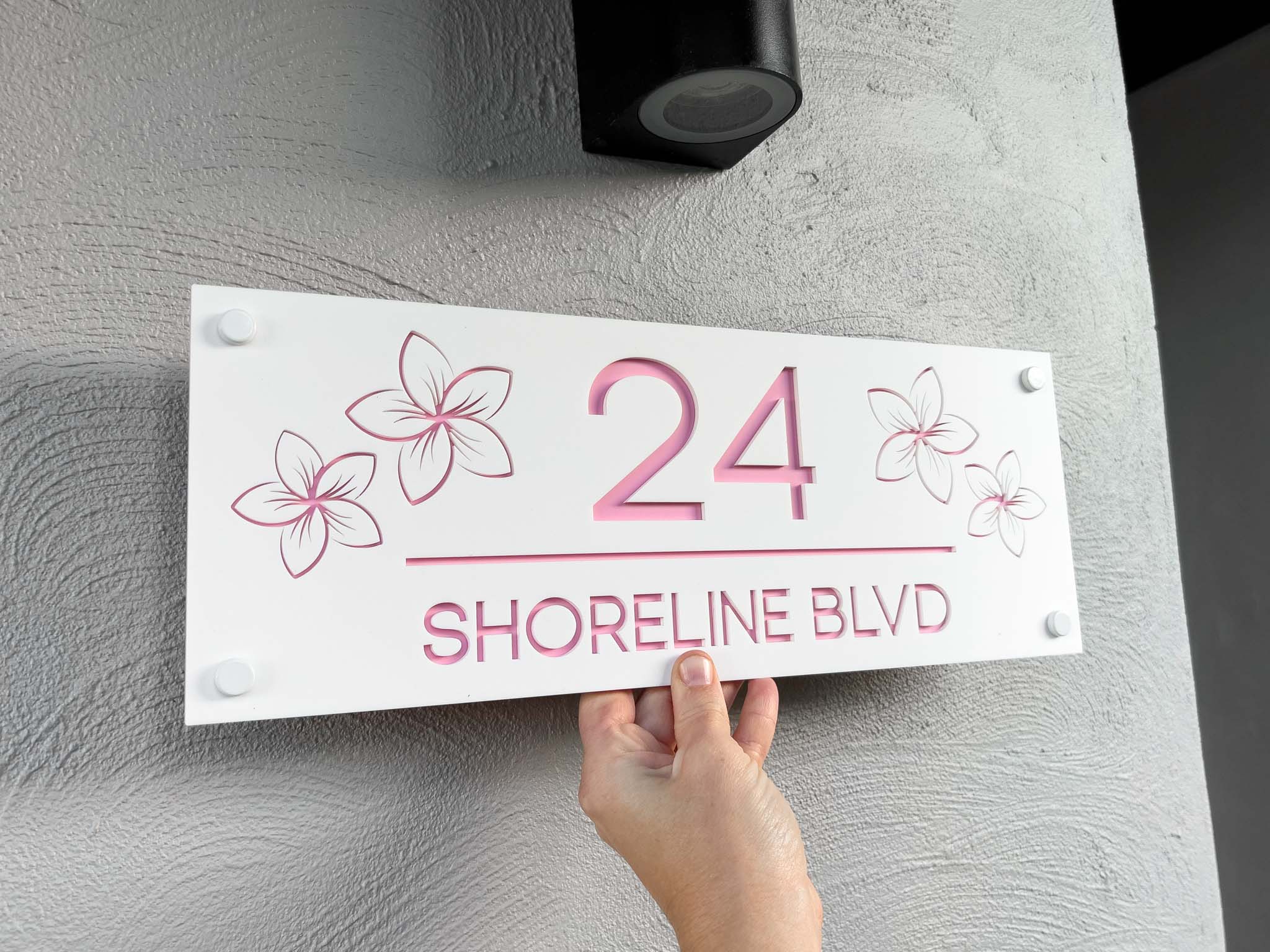 Tropical resort-style frangipani house sign that reads '24 Shoreline Blvd' in white and light pink.