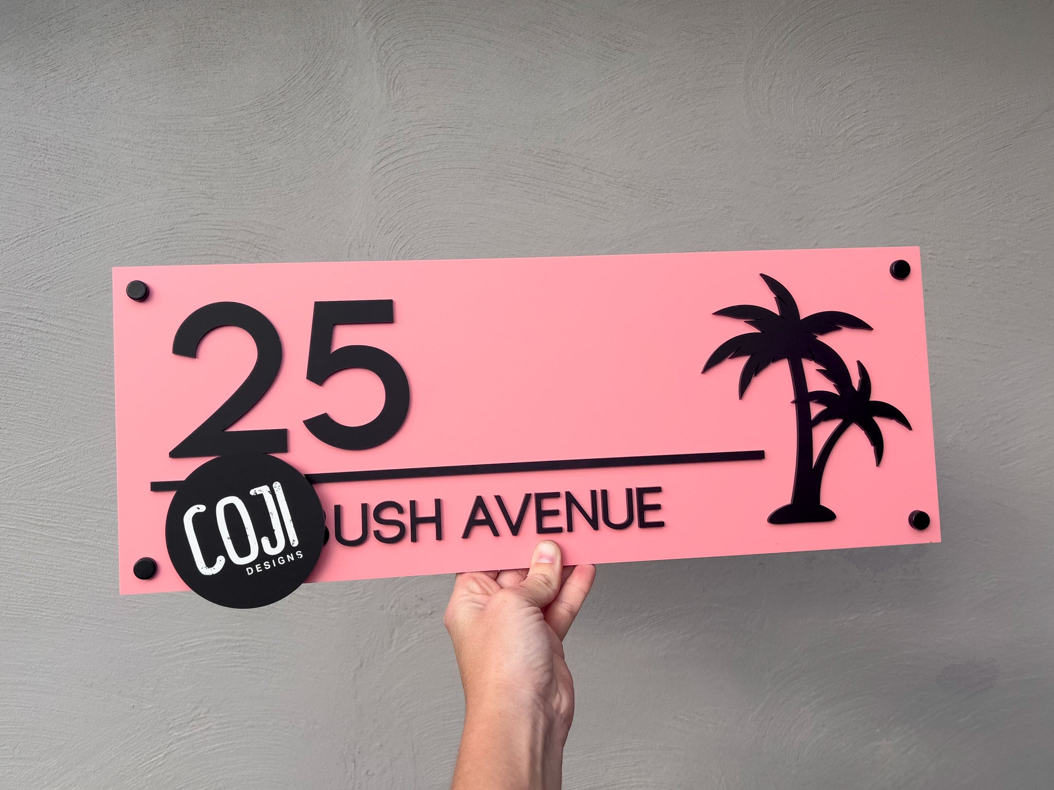 Melon pink and black peronsalised house sign with an address that reads '25 Avenue' with black wall mounts.