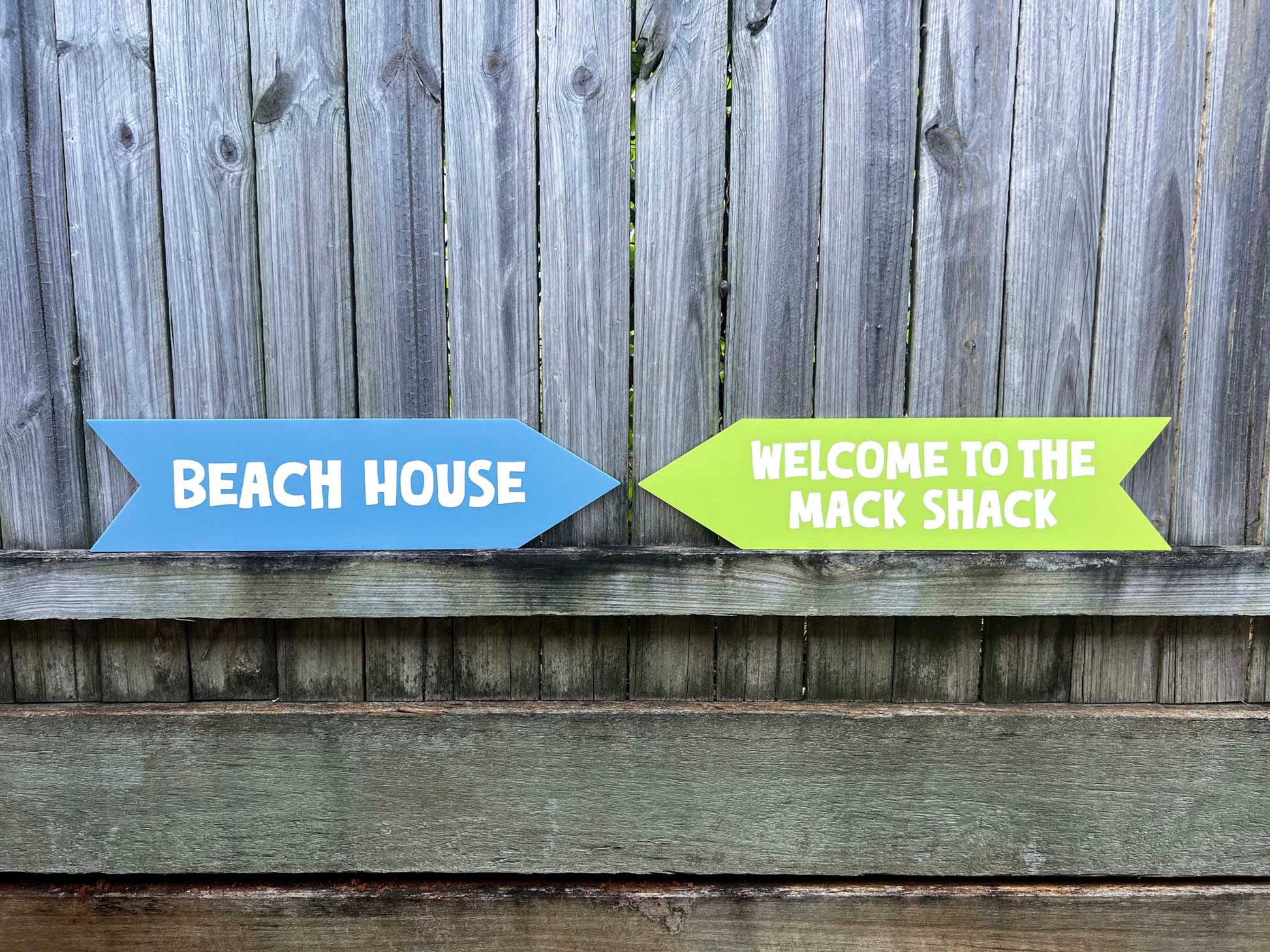 Two custom UV printed acrylic directional signs, one blue and one green, on a wooden surface with a wooden fence background.