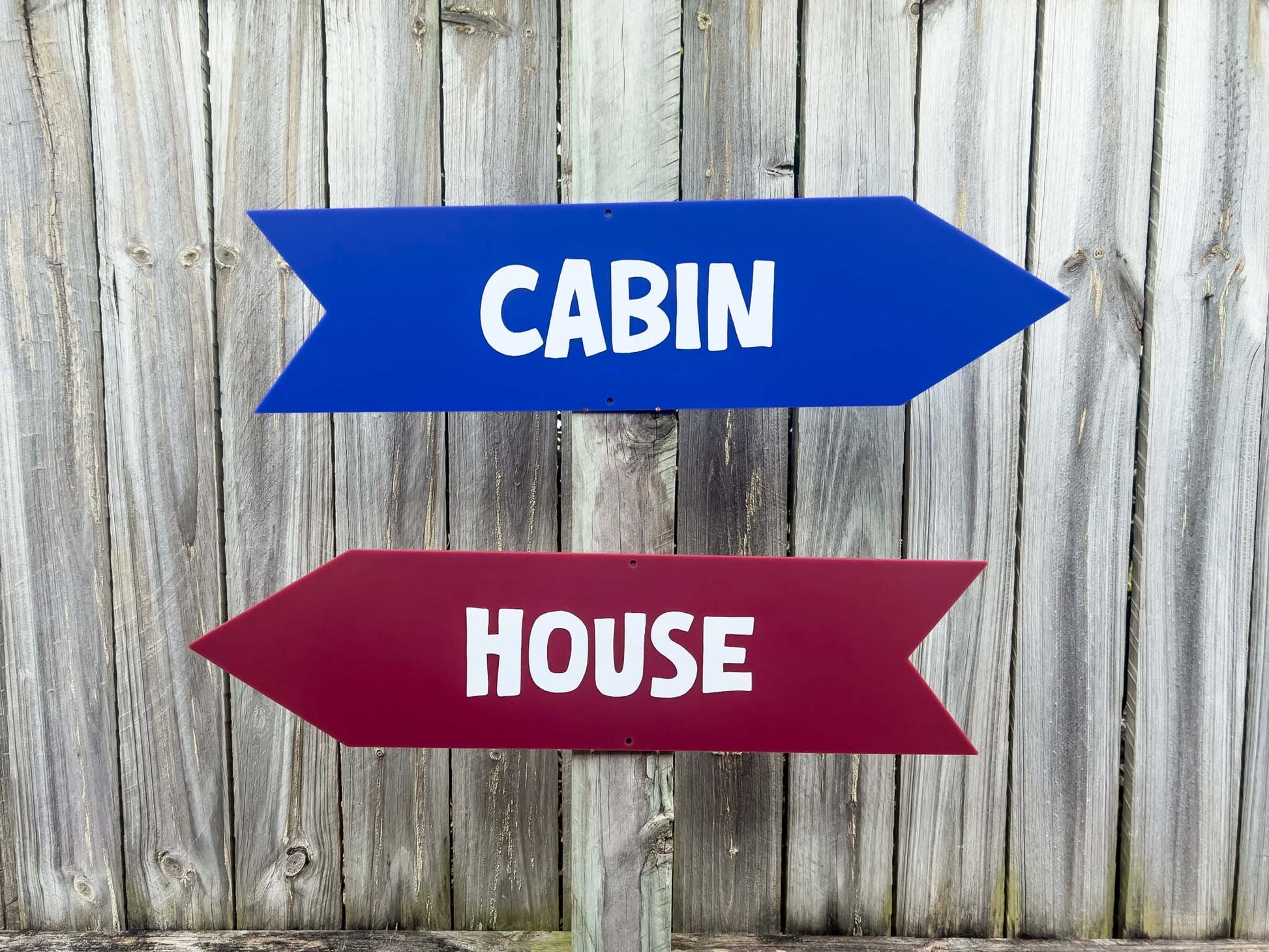 Two direction arrow signs in blue and maroon that say 'CABIN' & 'HOUSE'.