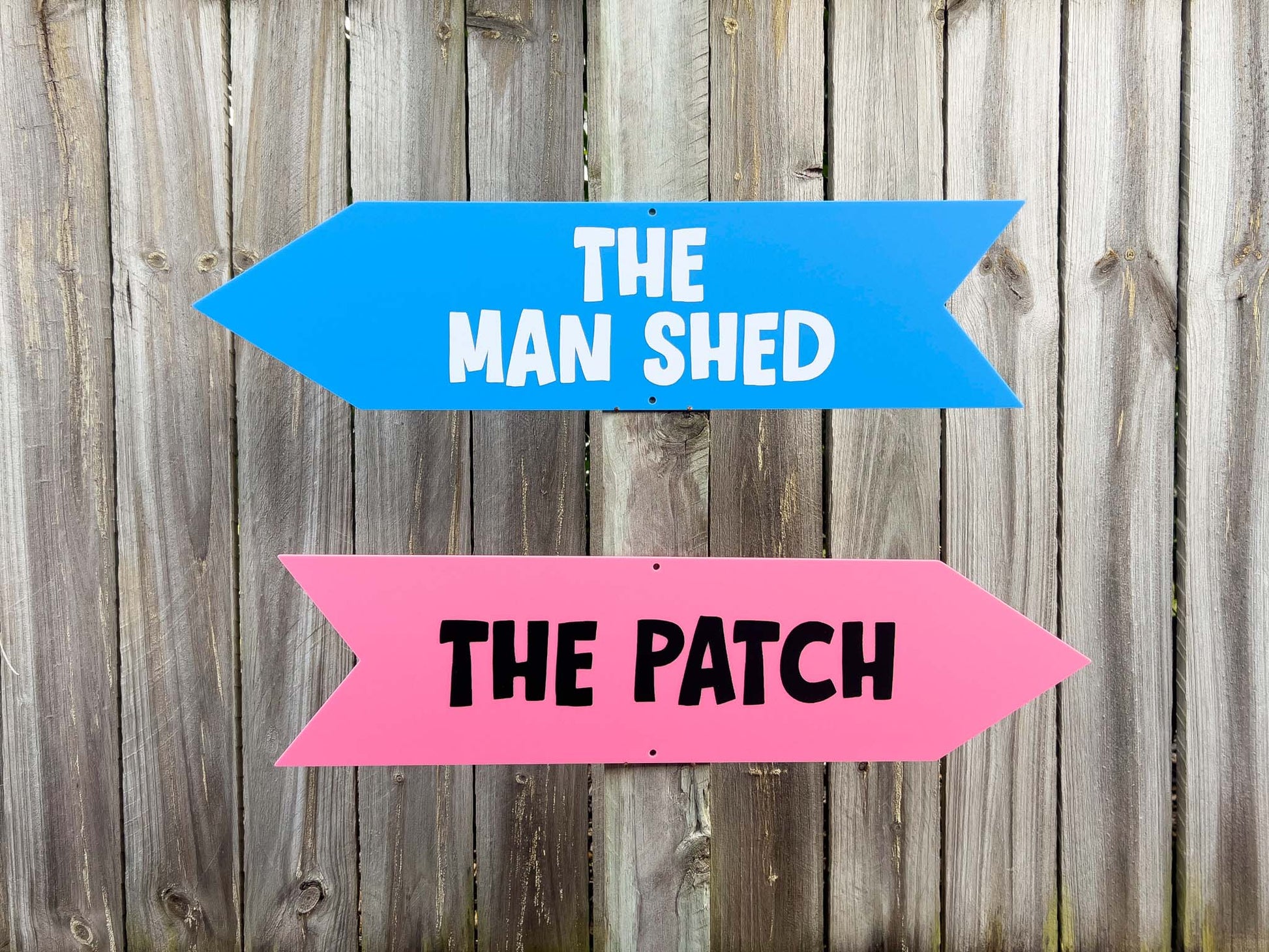 Two directional signs pointing to 'The Man Shed' and 'The Patch' on a wooden background.