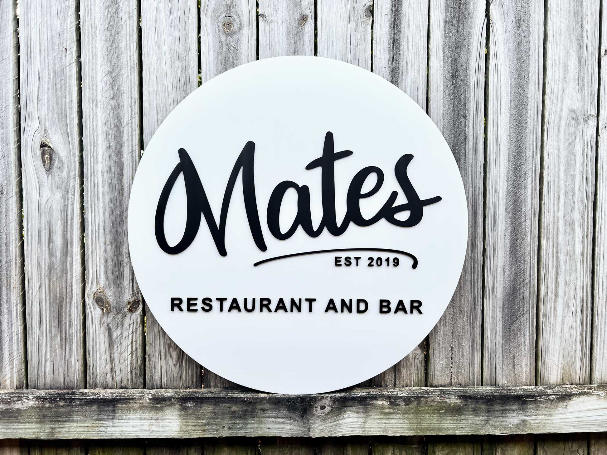 Round personalied 3D acrylic sign with 'Mates Restaurant and Bar' sitting on a wooden background.