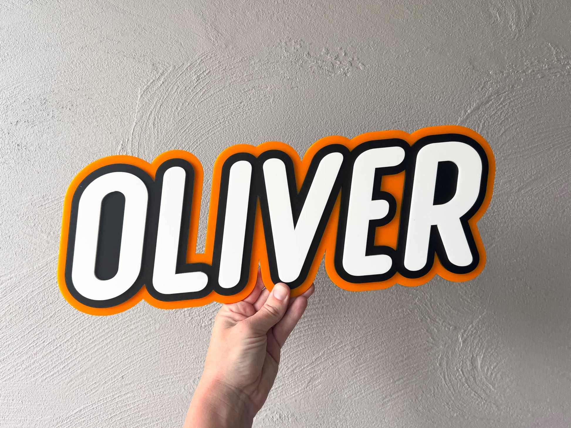 Bright coloured acrylic name plaque that says 'Oliver' in orange, black and white text.