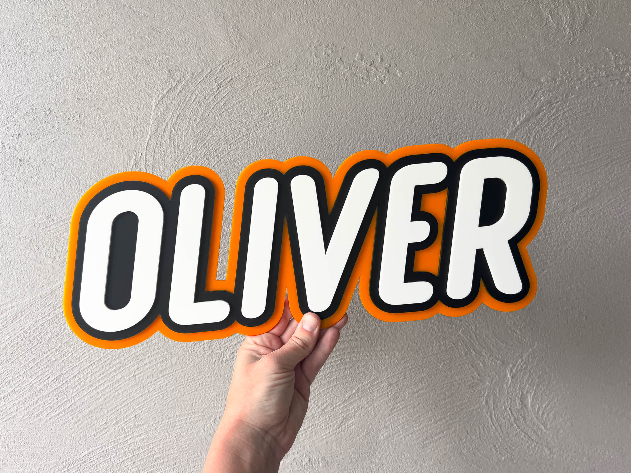 Bright coloured acrylic name plaque that says 'Oliver' in orange, black and white text.