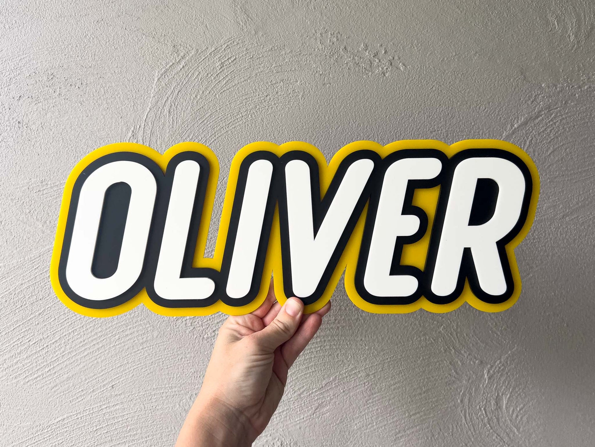 Custom 3D acrylic tripe layer name plaque in yellow, black and white that says 'Oliver'.