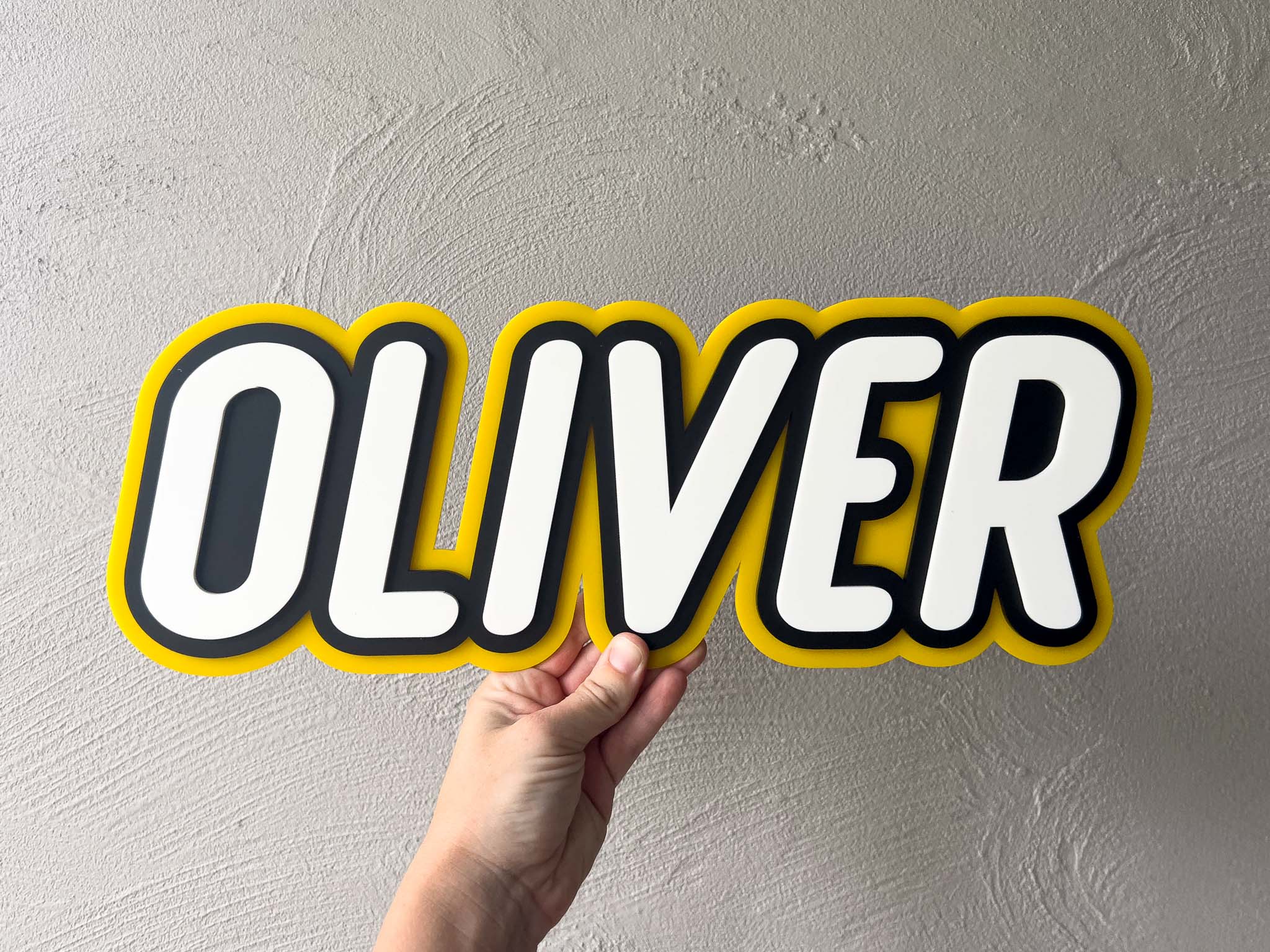 Custom 3D acrylic tripe layer name plaque in yellow, black and white that says 'Oliver'.