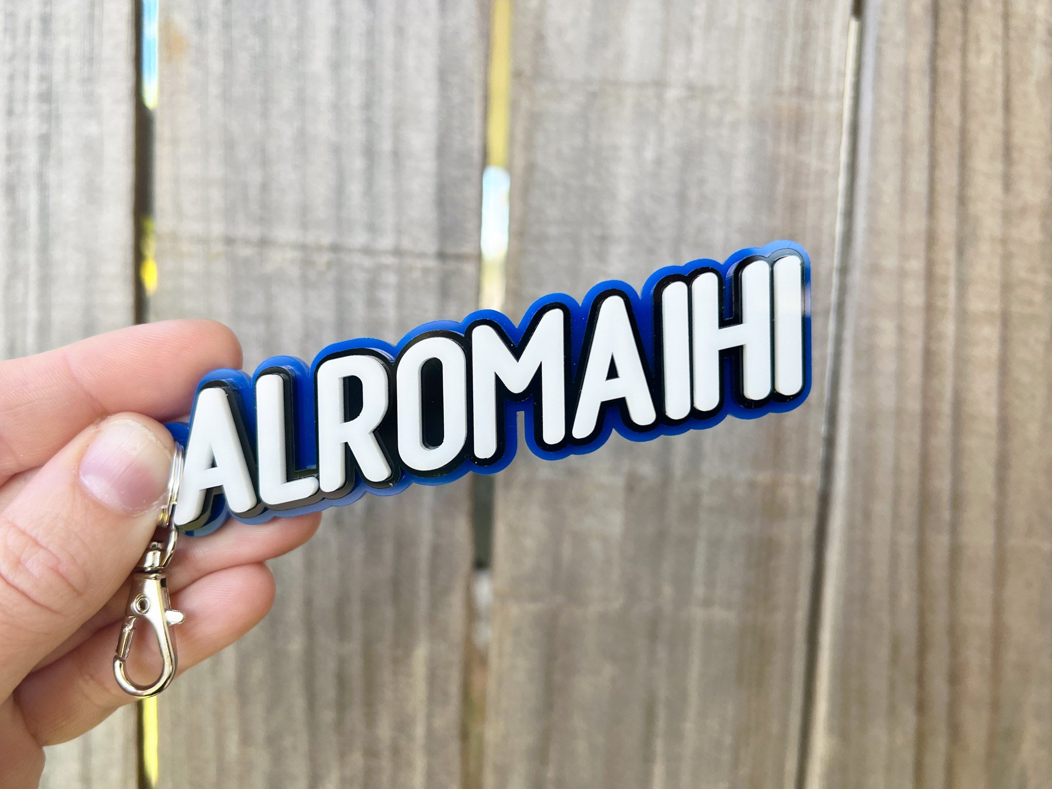 Keychain with 'ALROMAIHI' text held against a wooden background