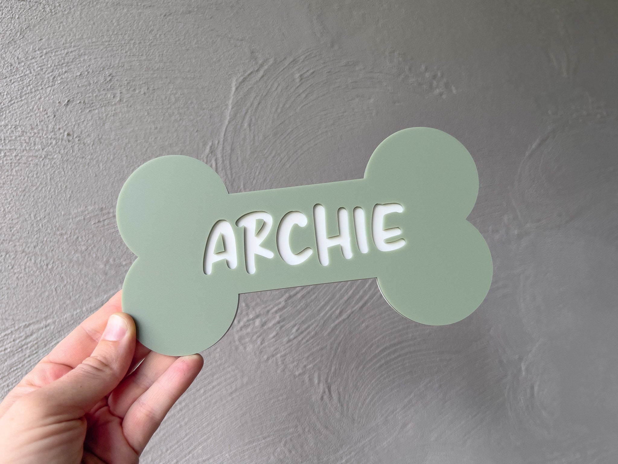 Hand holding a green bone-shaped sign with 'ARCHIE' on a gray background