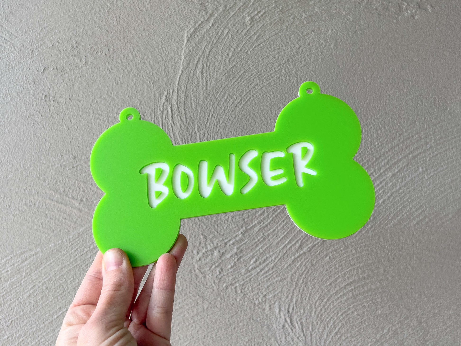 Green bone-shaped sign with 'BOWSER' text held against a gray wall.