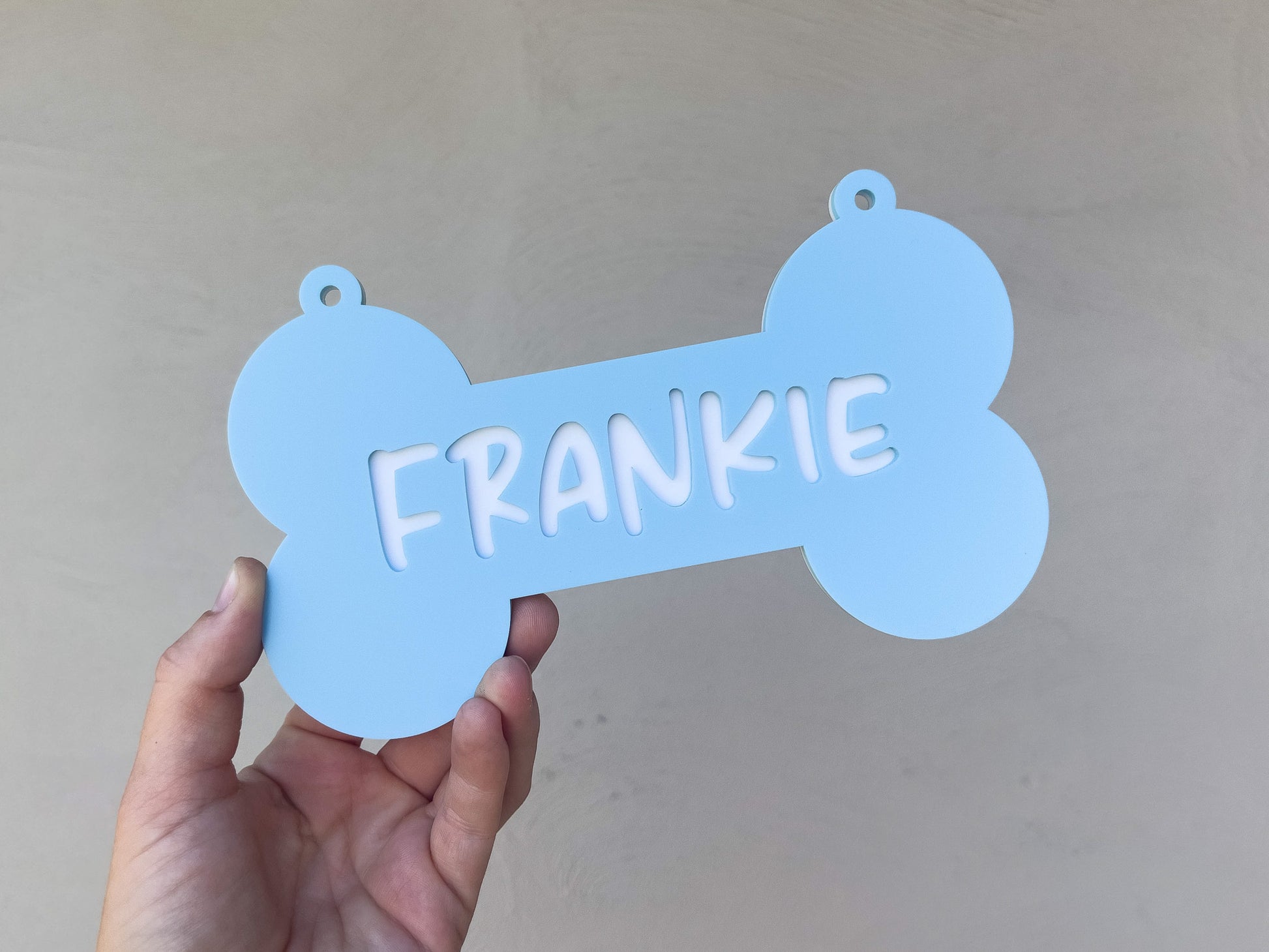 Blue bone-shaped pet tag with 'FRANKIE' on a plain background
