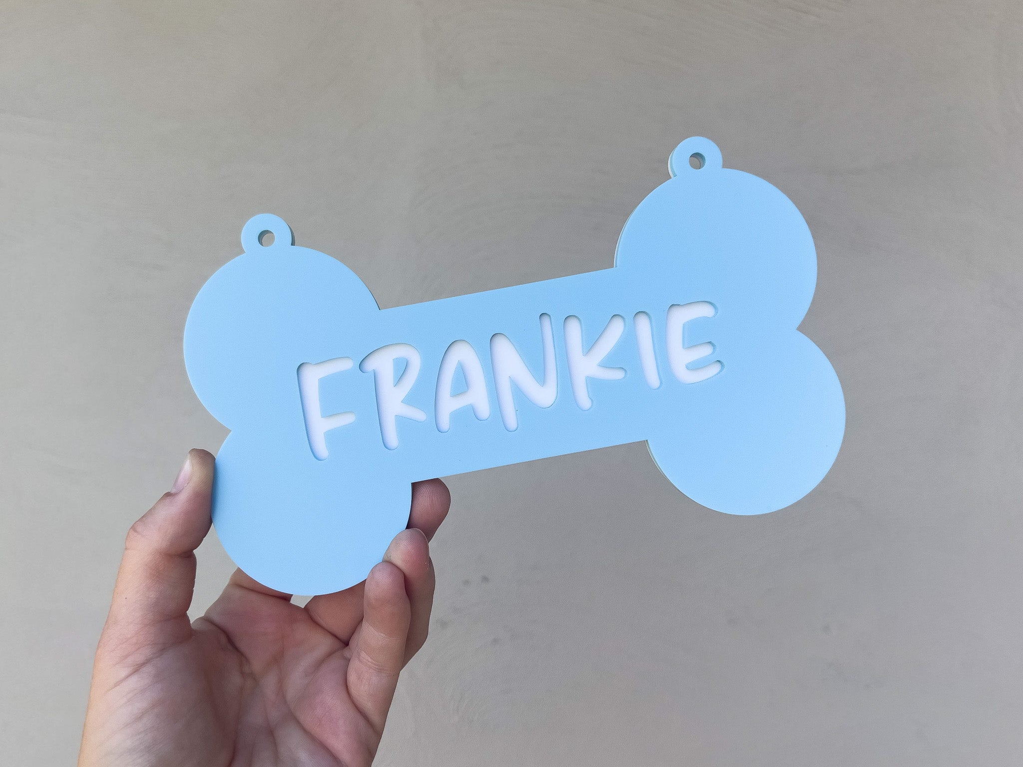 Blue bone-shaped pet tag with 'FRANKIE' on a plain background
