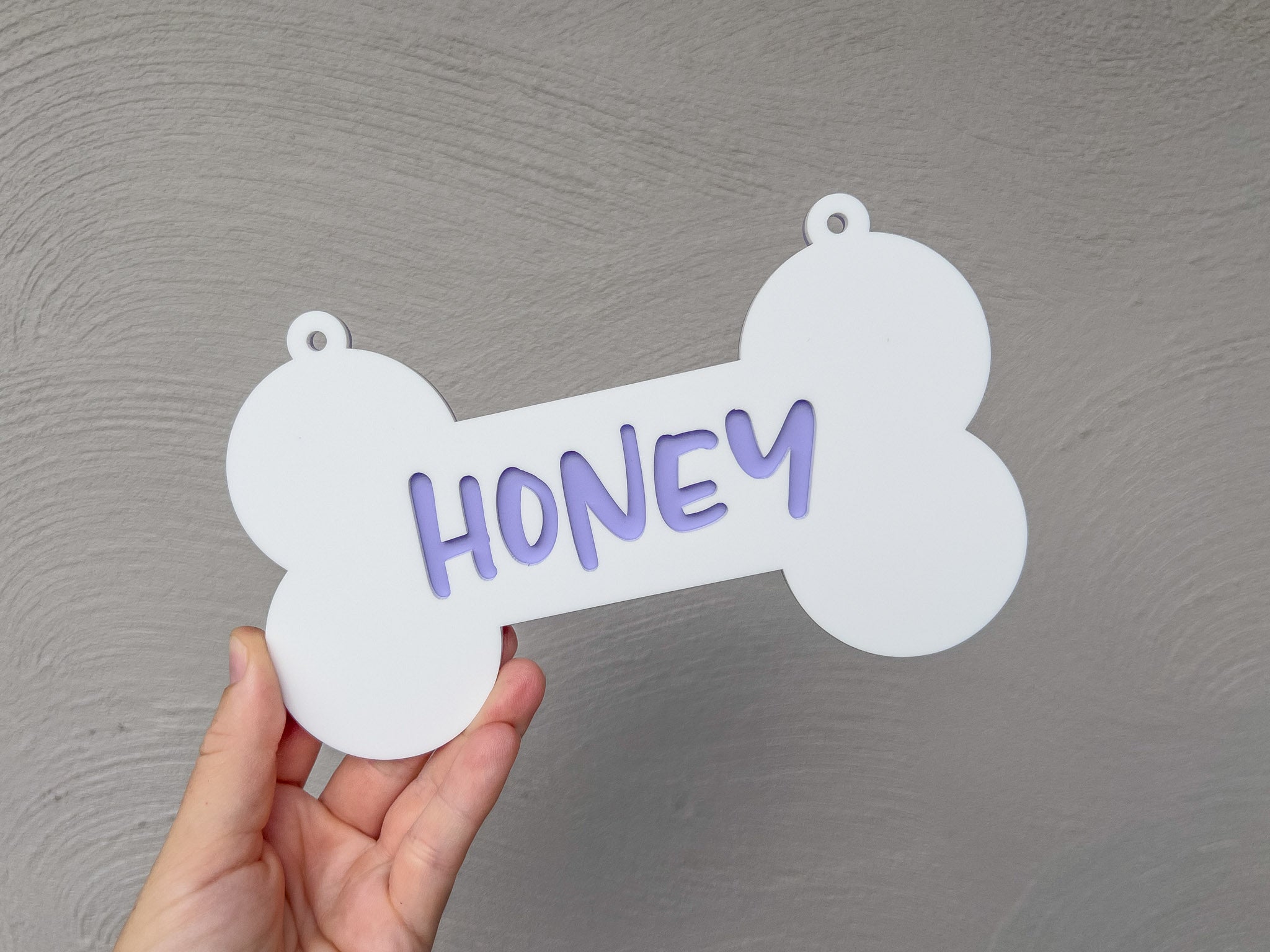 Hand holding a bone-shaped sign with 'HONEY' written on it against a gray background | Coji Designs