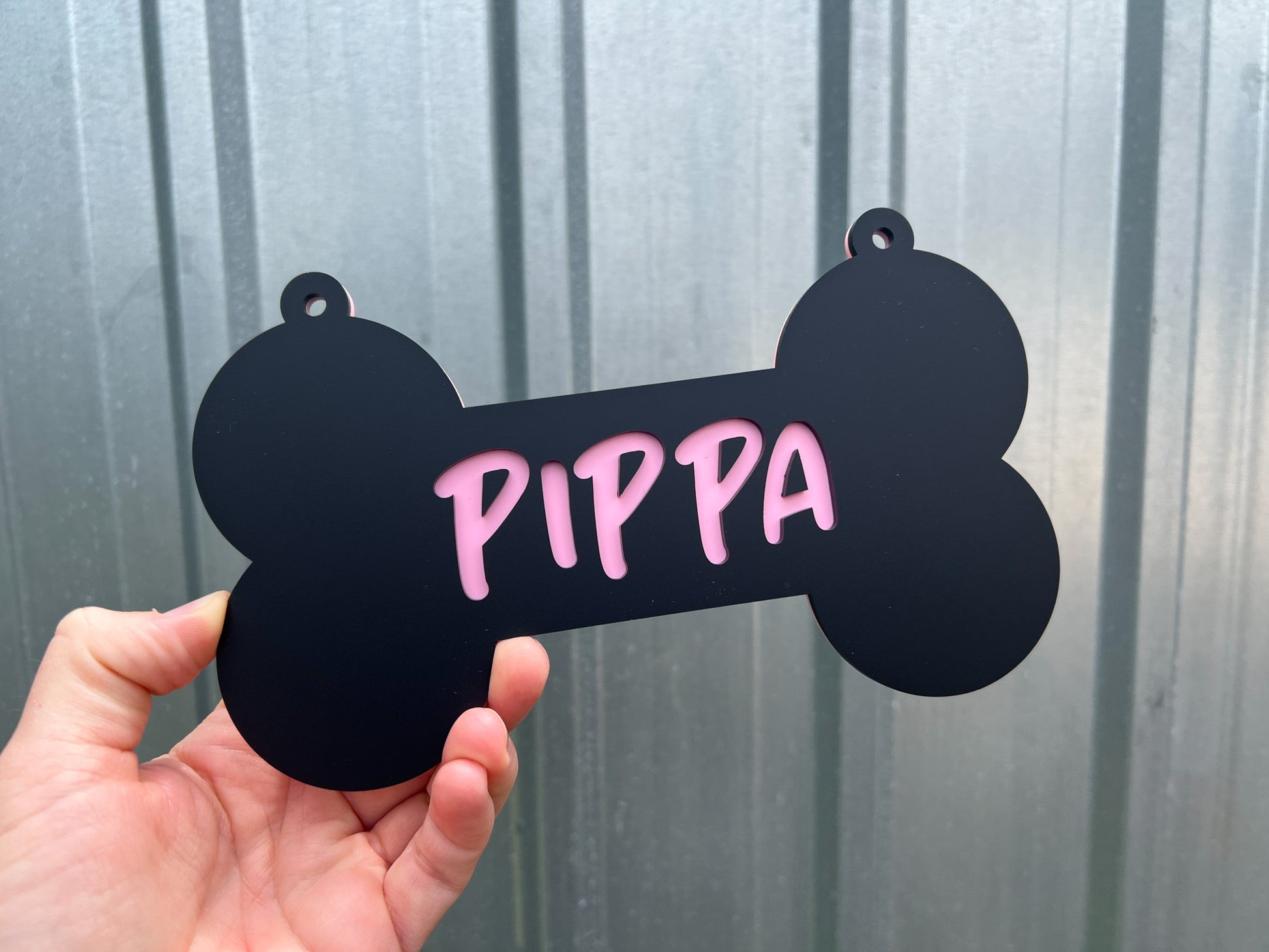 Black bone-shaped tag with 'PIPPA' written in pink held against a metallic background | Coji Designs