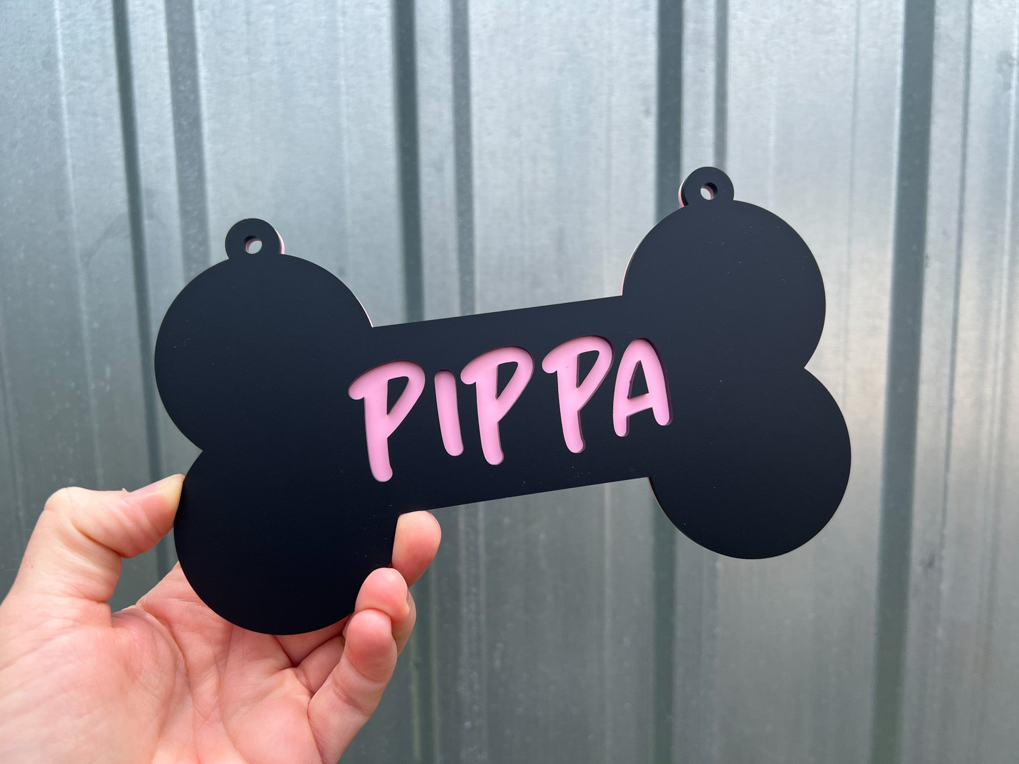 Black bone-shaped tag with 'PIPPA' written in pink held against a metallic background | Coji Designs