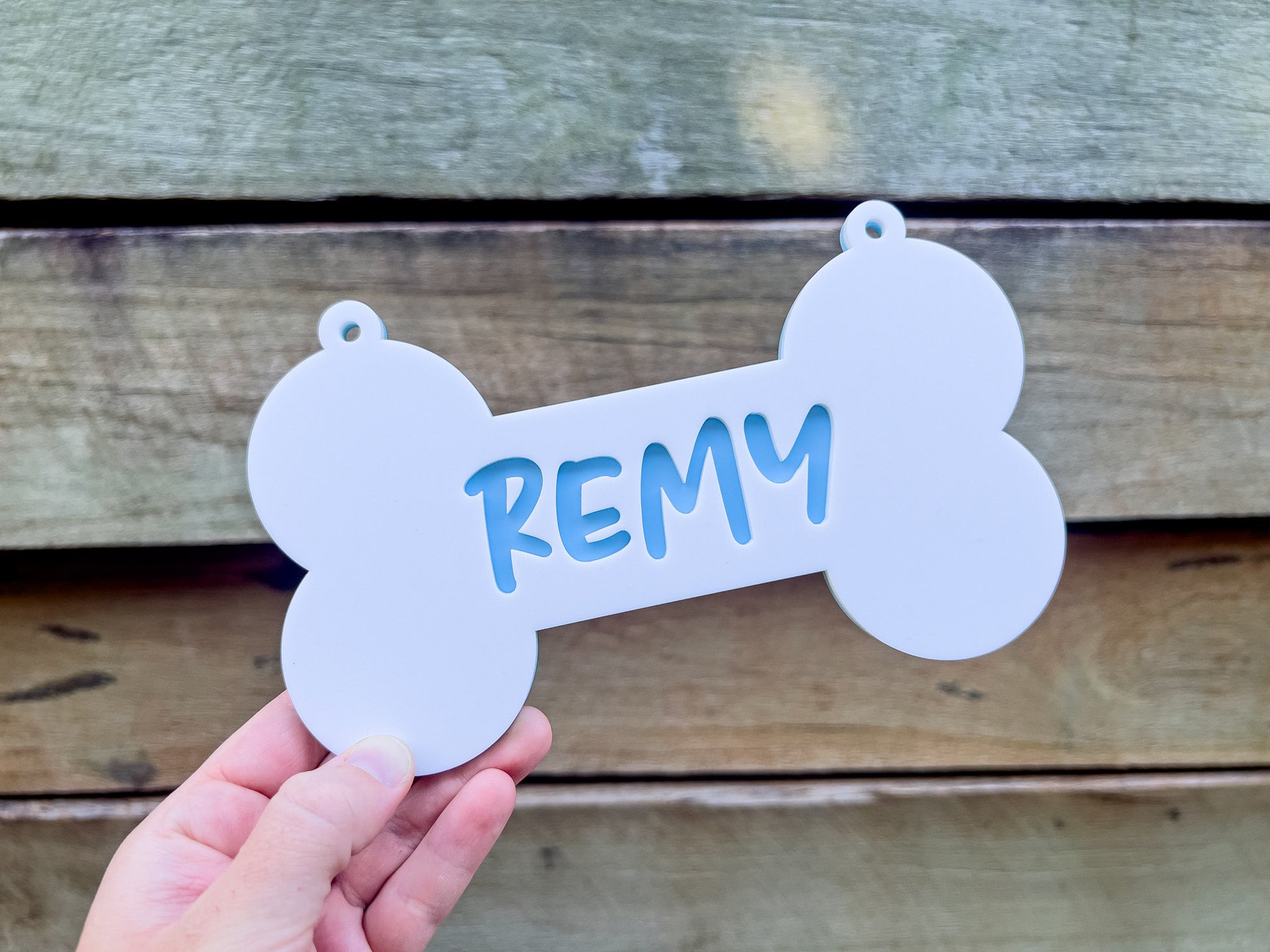 White bone-shaped tag with 'REMY' written on it, held against a wooden background.