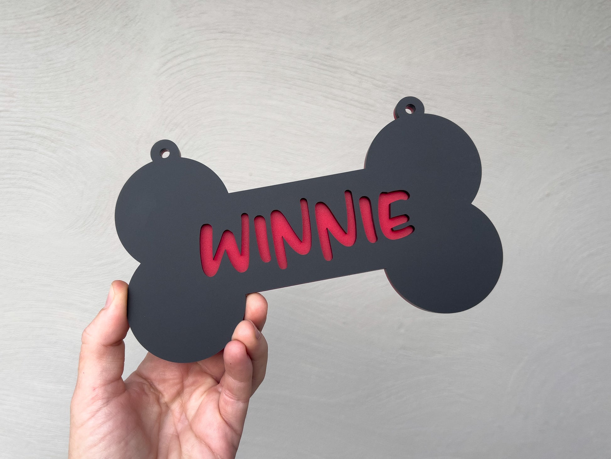 Black bone-shaped tag with 'Winnie' in red text held by a hand against a light gray background | Coji Designs