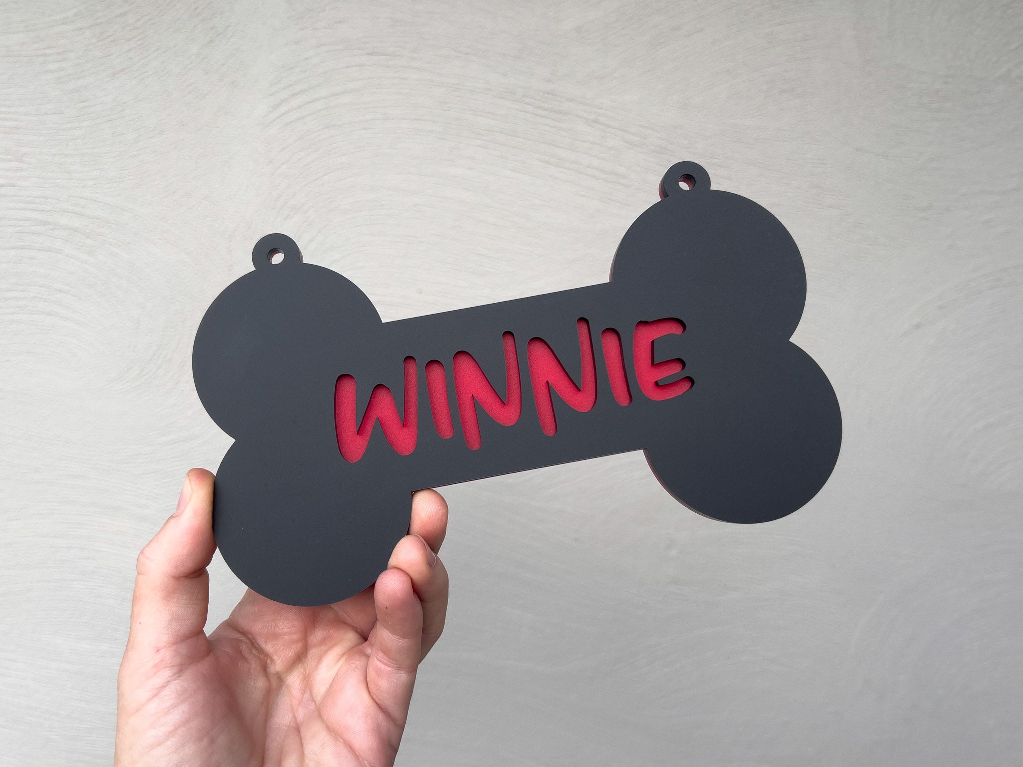 Black bone-shaped tag with 'Winnie' in red text held by a hand against a light gray background | Coji Designs