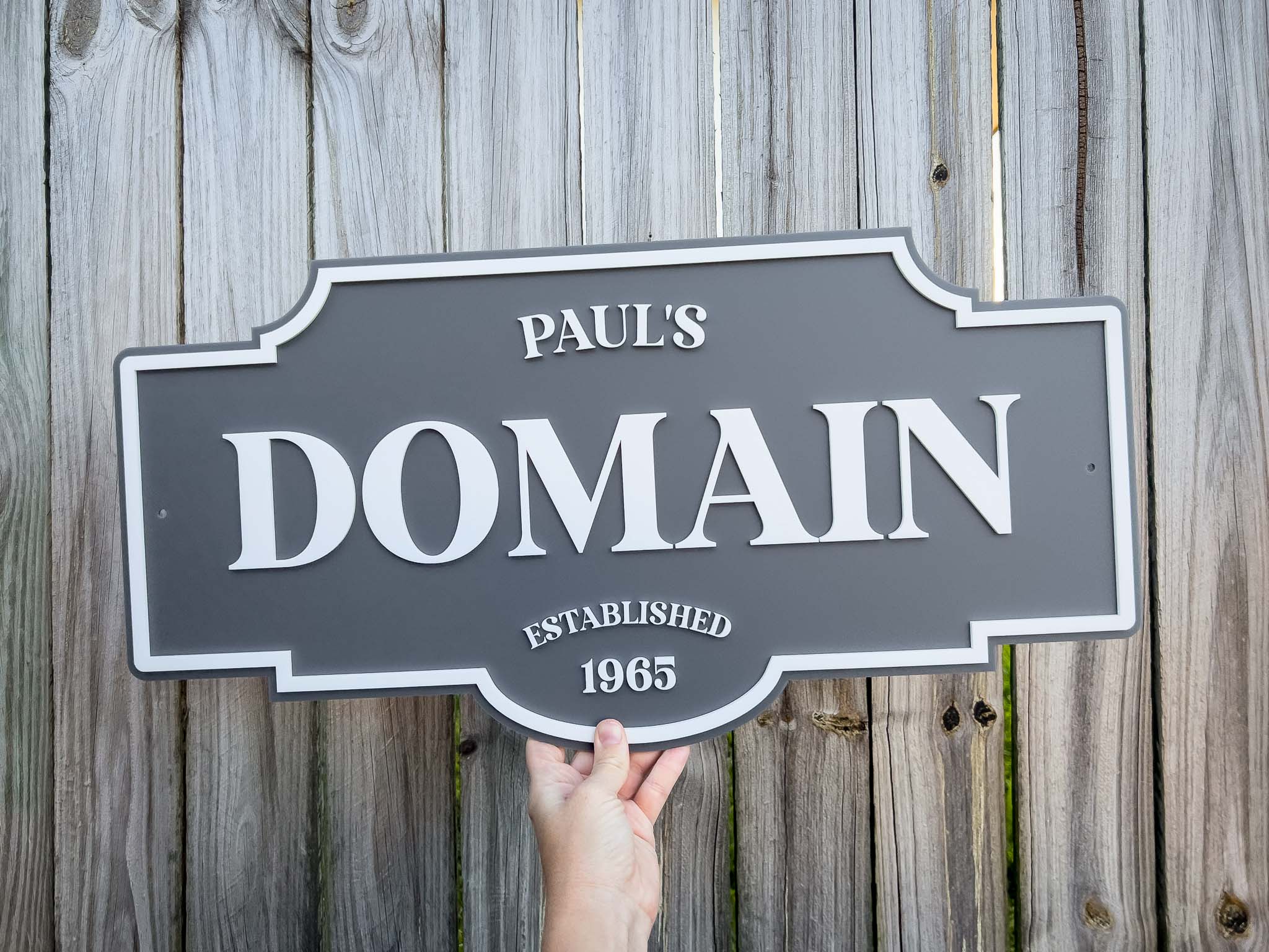 Hand holding a sign with 'Paul's Domain Established 1965' against a wooden background