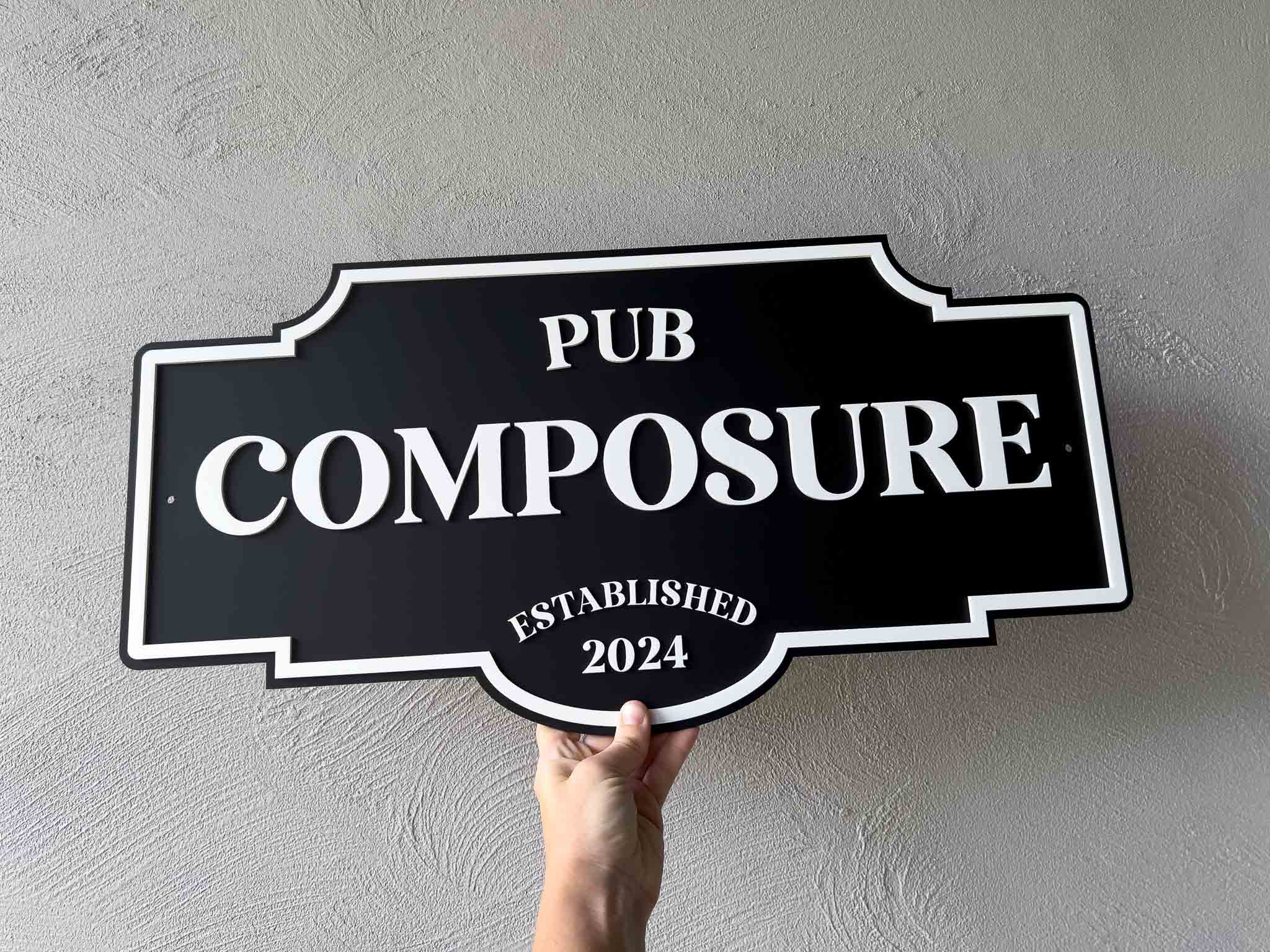 Black and white custom made classic sign with 'Pub Composure Established 2024' against a plain background