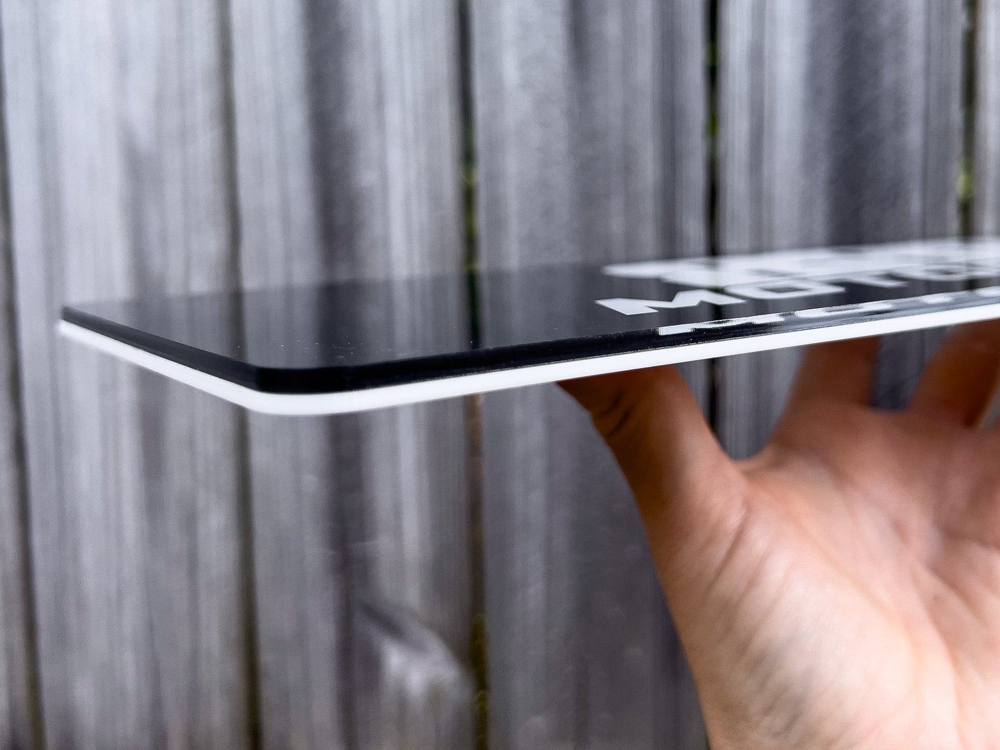 Hand holding a side view of a glossy double layer acrylic logo plate